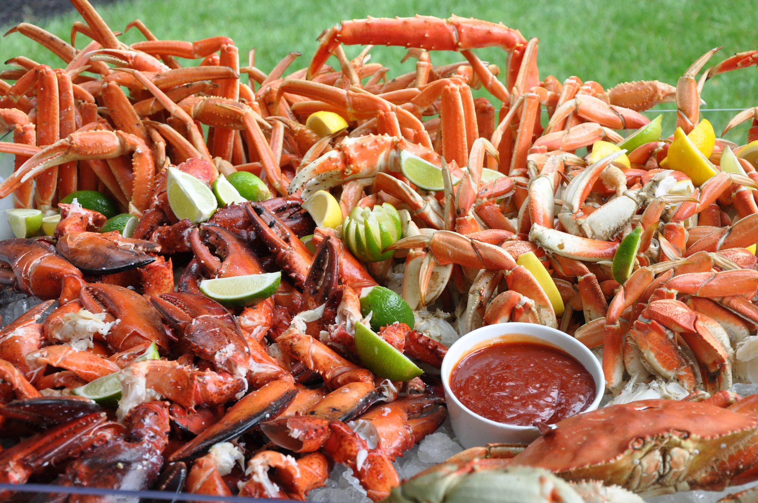 A seafood platter featuring cooked crabs and lobsters, garnished with lime and lemon wedges, served with a spicy dipping sauce.