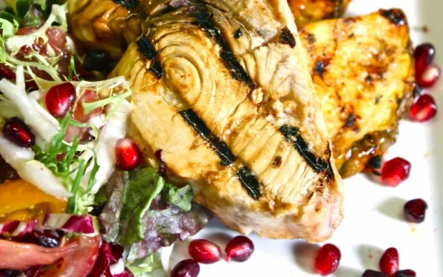 Grilled chicken breast with grill marks, served with salad and pomegranate seeds