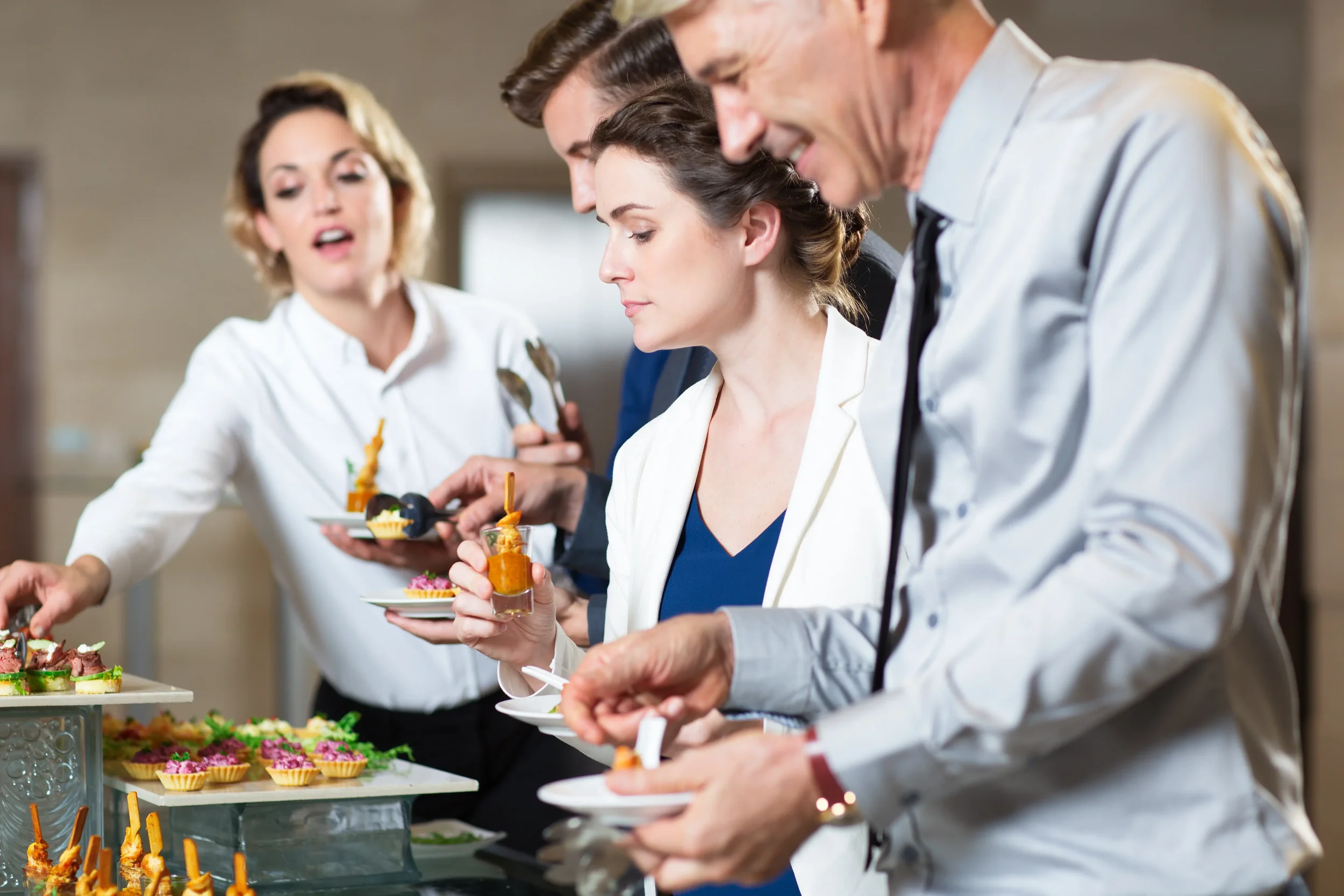 Group of people serving themselves from a buffet table with various appetizers and desserts.