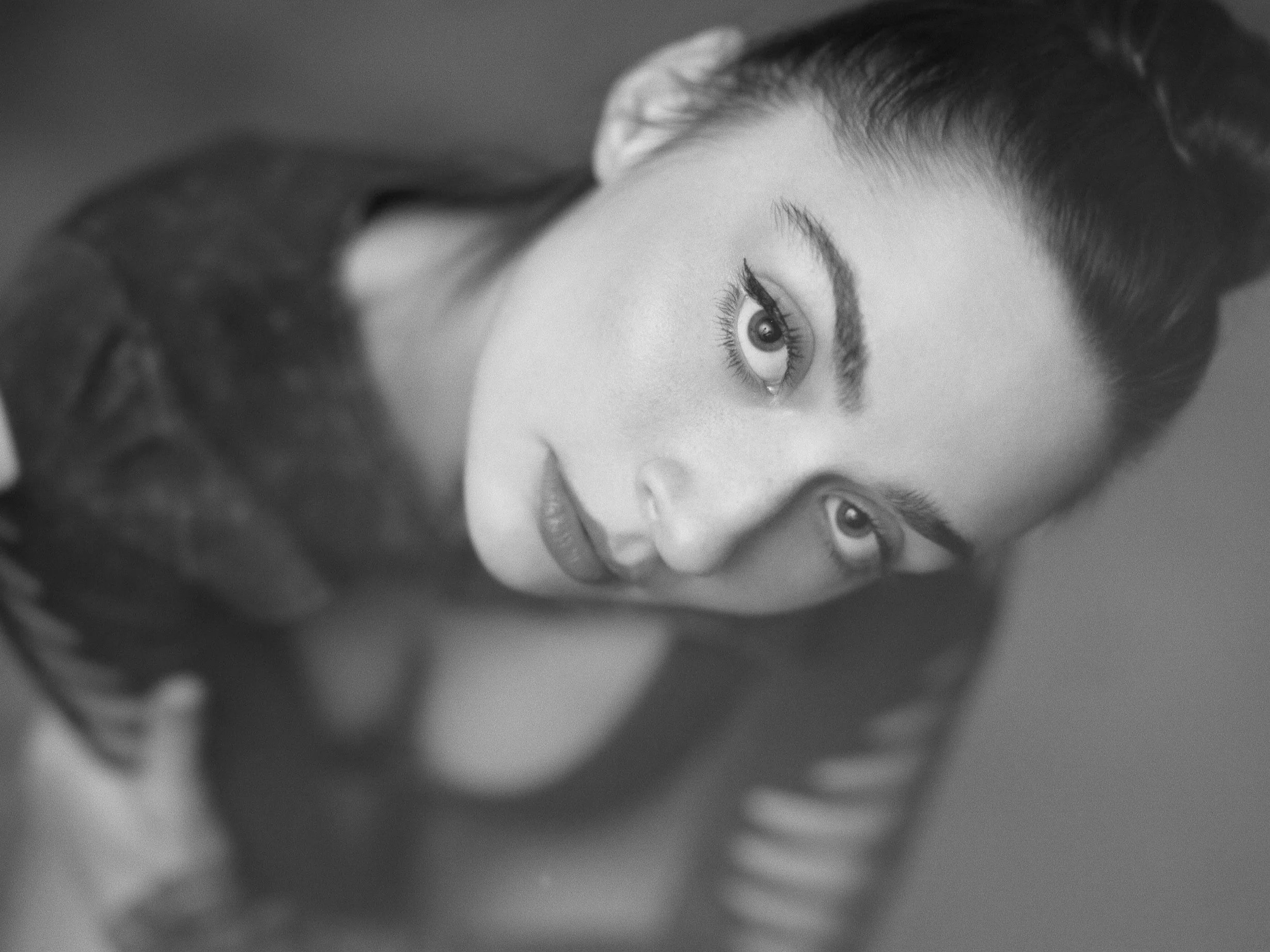 A black and white portrait of a woman with styled hair, lying down, looking at the camera.