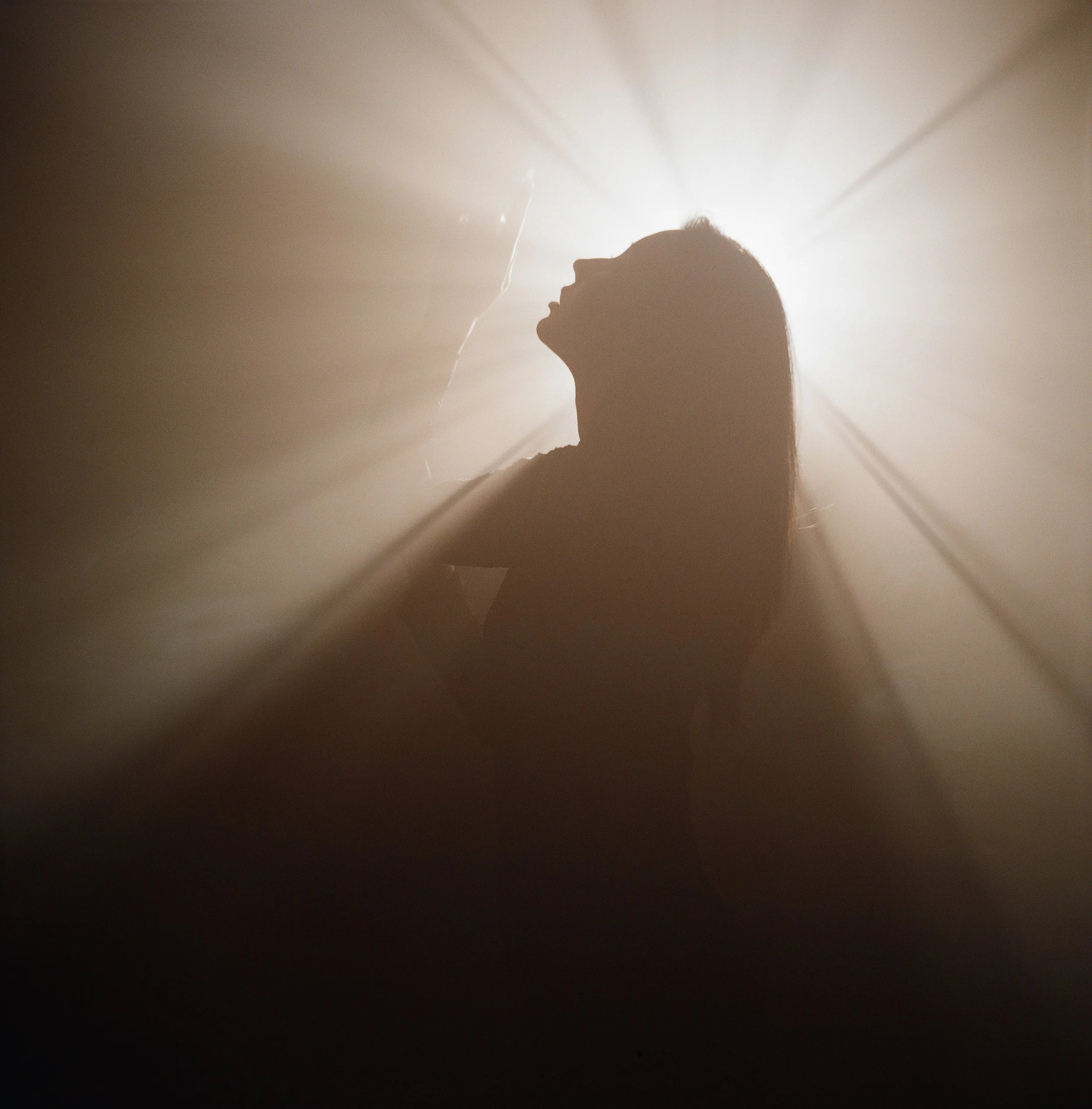 Silhouette of a woman with long hair against a backlit, hazy background.