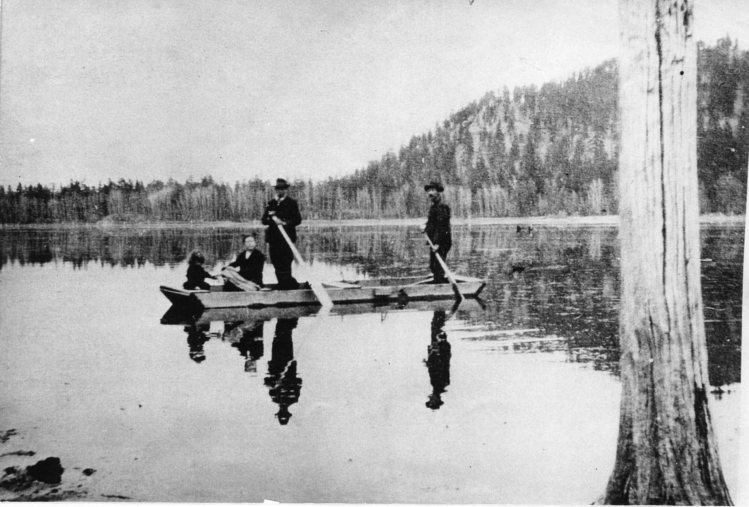 Left to right: Linnie Munro (Hale), Mrs. Findlay Munro, Findlay Munro, and Philip Munro paddling a flat bottom boat on Fish Lake.