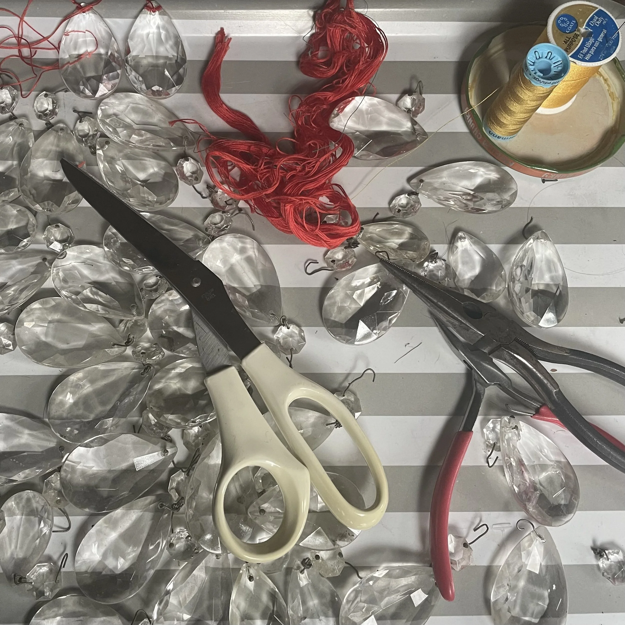 Assorted glass beads, red and yellow embroidery thread, and sewing tools such as scissors and needles on a striped surface.