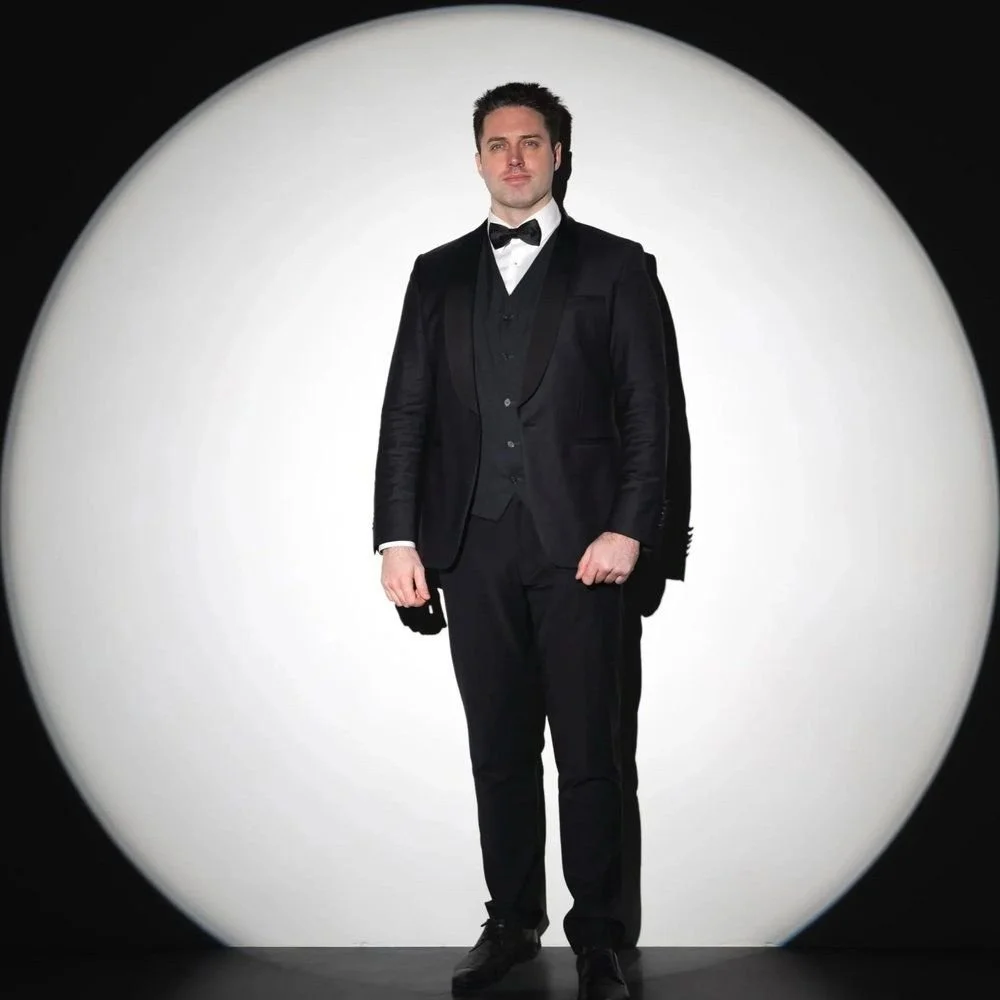 Tobias Greenhalgh in a tuxedo, standing in a white spotlight