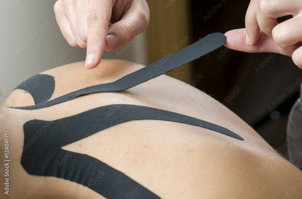 Close-up of a person applying black decorative tape or body tape to the skin around the shoulder and upper arm area.