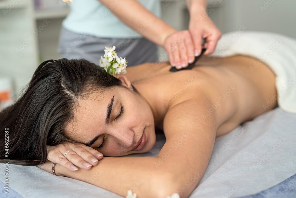 A woman receiving a back massage in a spa setting, with a flower tucked behind her ear.