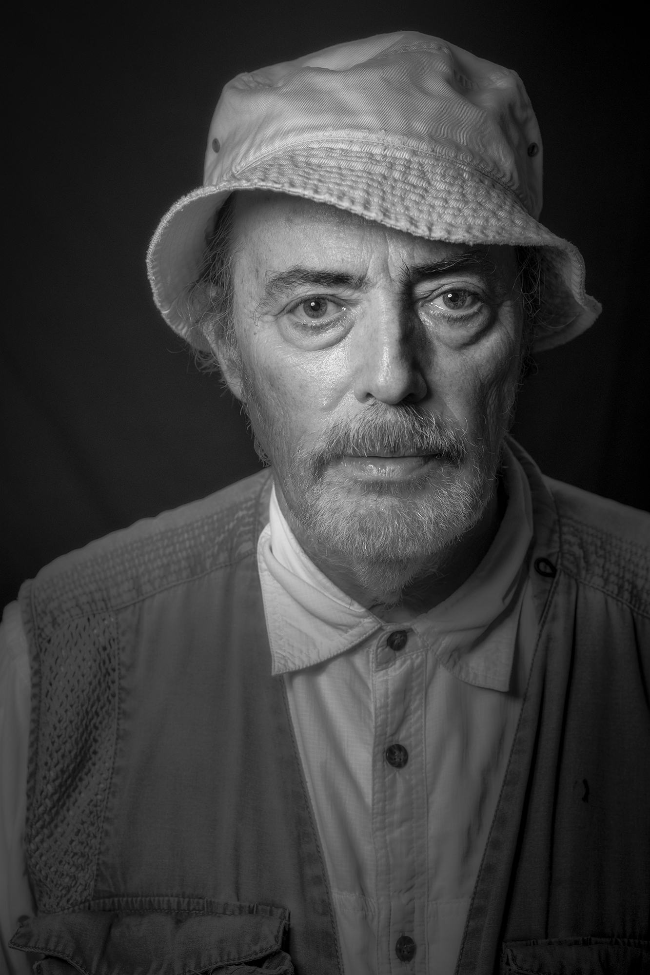 A black and white portrait of an elderly man wearing a wide-brimmed hat and a button-up shirt. Bruce Gilden by Kent Corley
