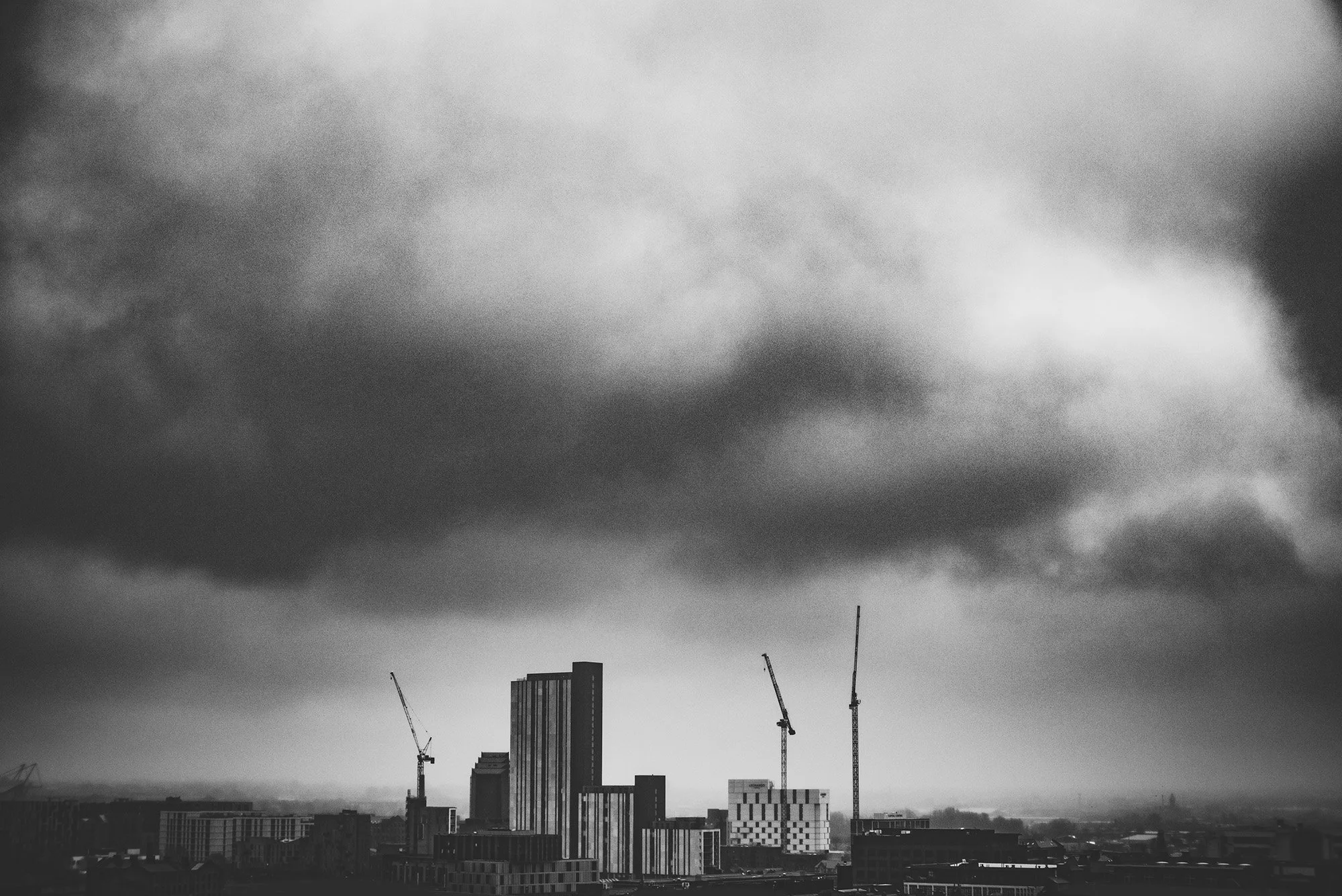 Ominous clouds and cranes over Manchester, England. Dark and moody Black and White.  Kent Corley Photography