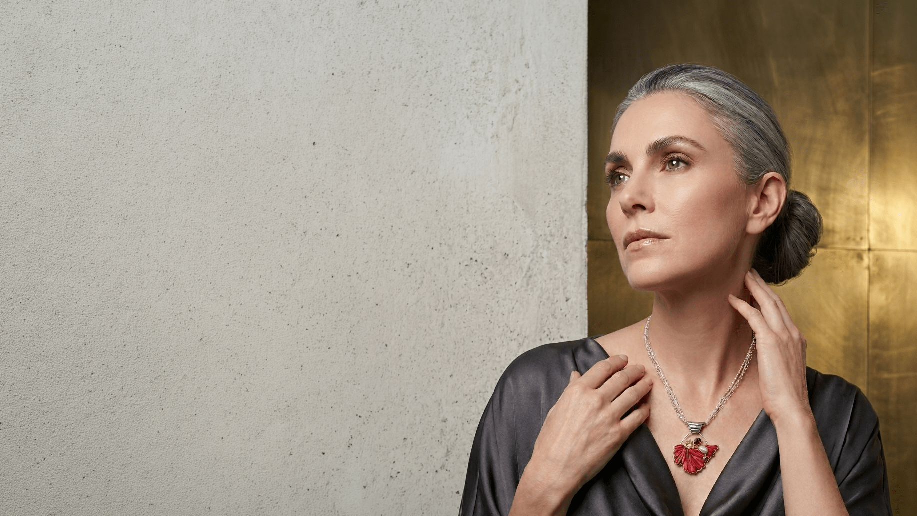 Elegant older woman with gray hair styled in a bun, wearing a black satin dress and a striking red art glass and gemstone necklace.