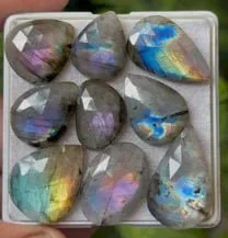 Tray of faceted moonstones in teardrop and oval shapes, flashing blue, violet, and gold.