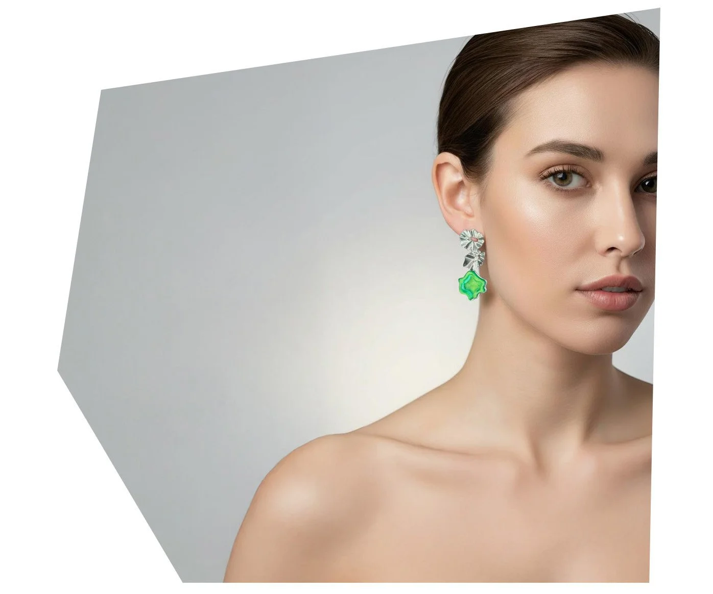 Close-up portrait of a woman with fair skin, short brown hair, wearing statement earrings with floral and green gemstone details, against a plain light gray background.