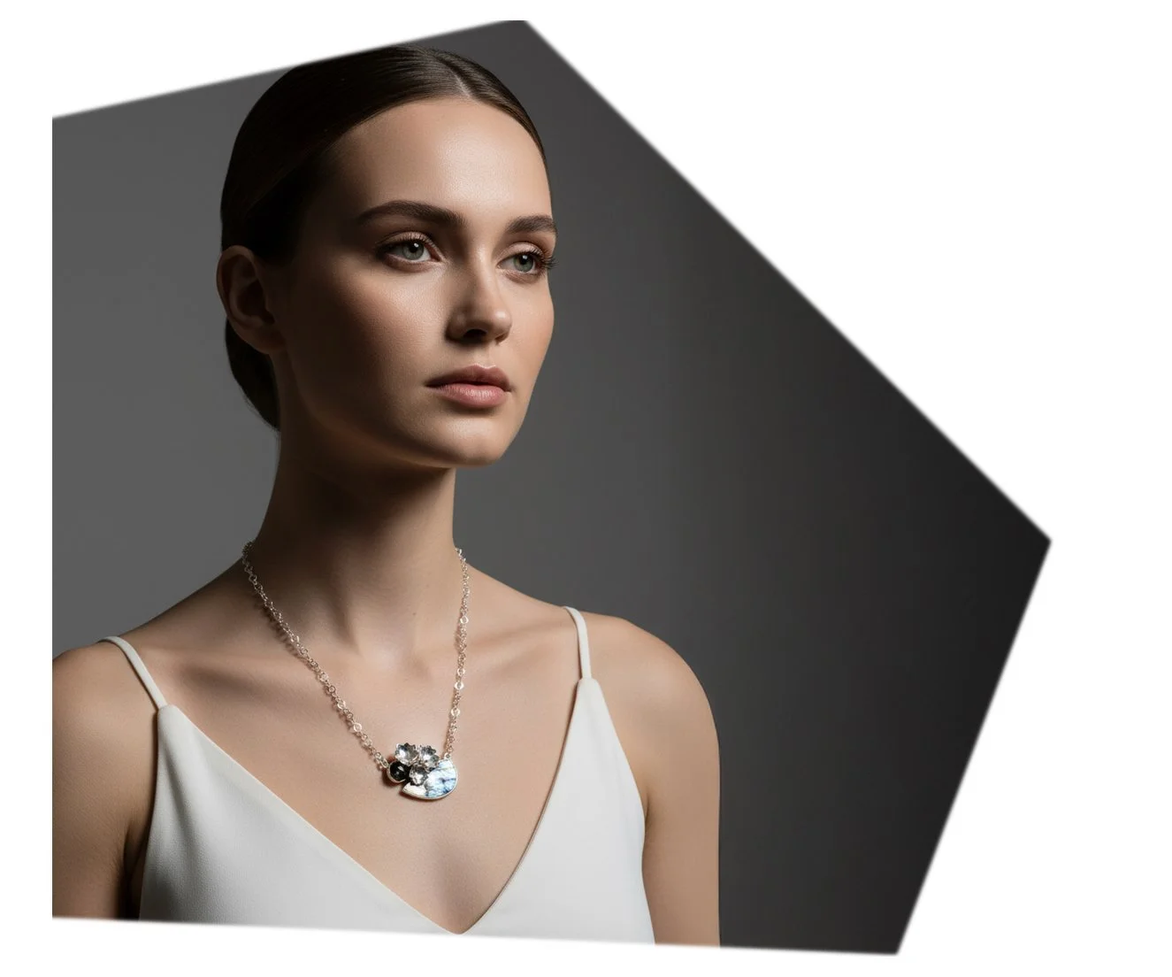 A woman with brown hair and fair skin wearing a white spaghetti strap top and a silver necklace with a pendant, looking to the side against a gray and white background.