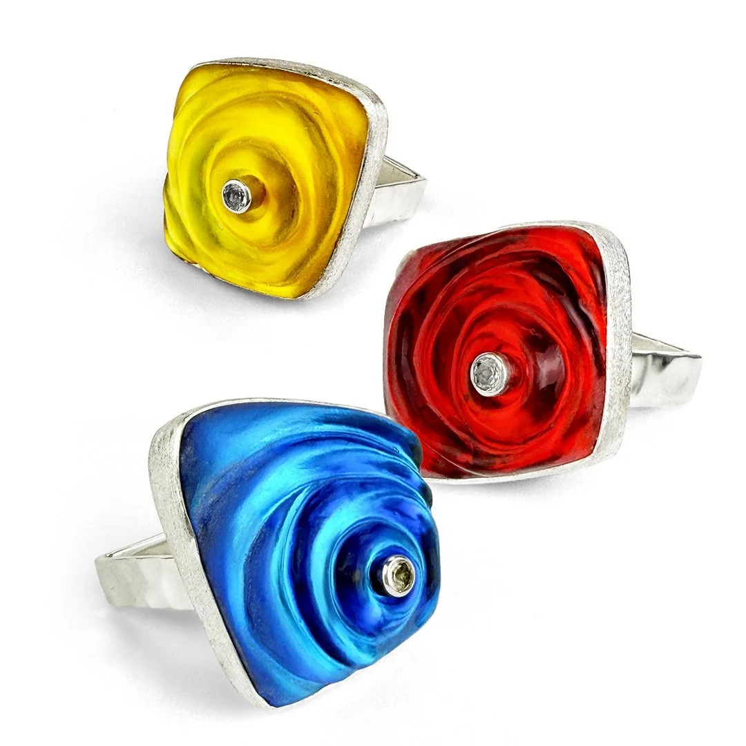 Handmade sterling silver rings with cold worked glass in yellow, red, and blue, each with a faceted white topaz center.