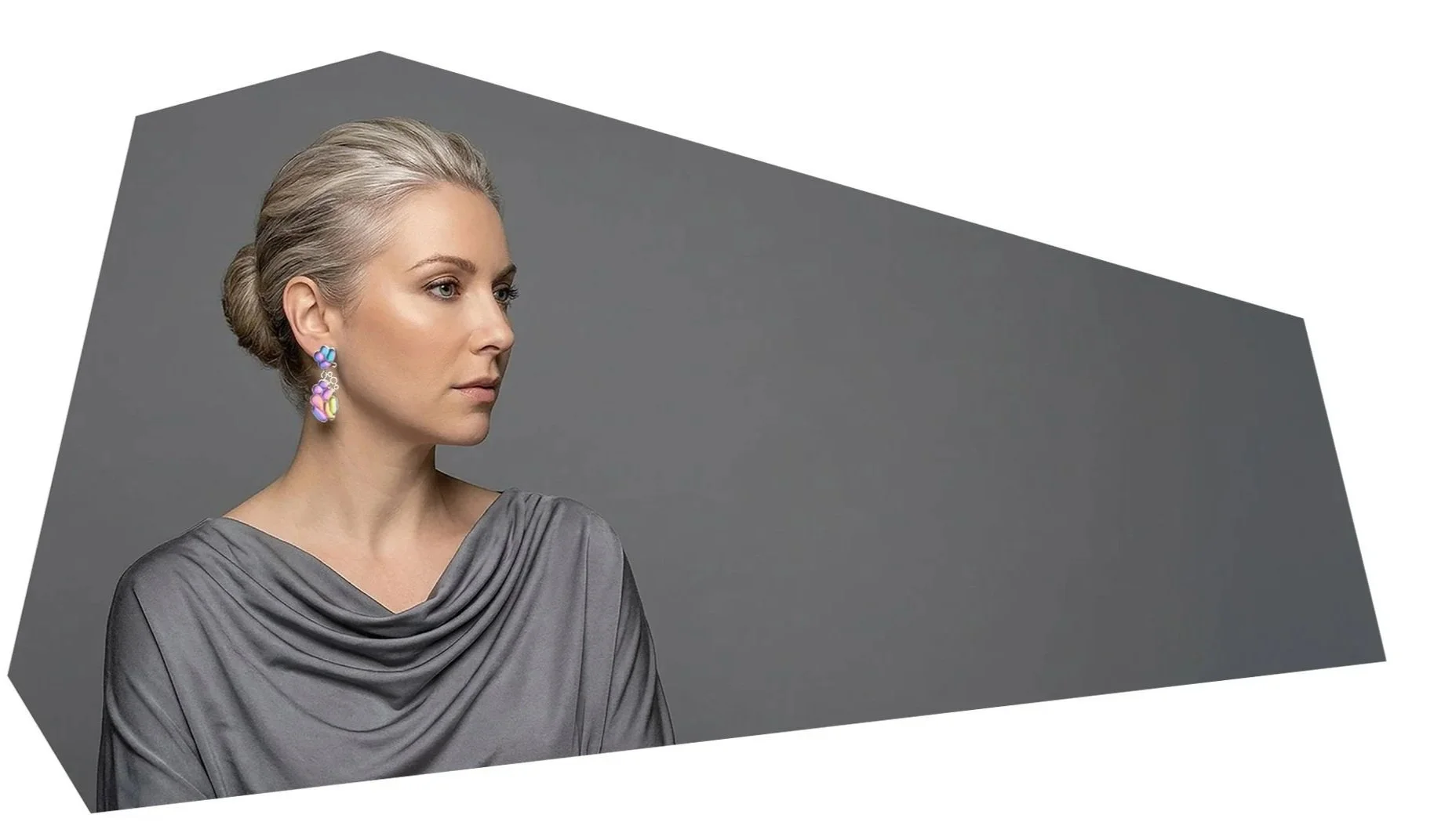 A woman with blonde hair tied back, wearing purple earrings and a gray satin draped dress, looking to the left against a gray background.