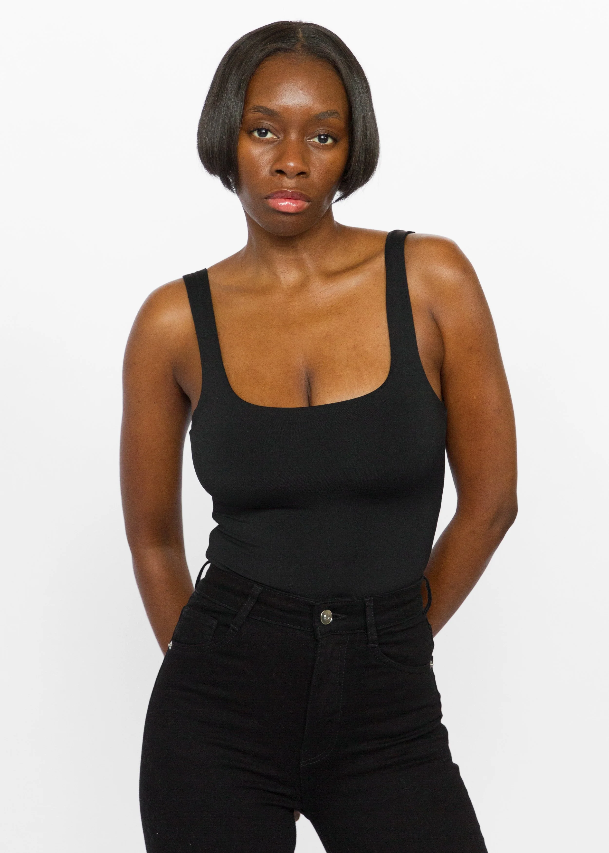 Portrait of a young woman with short black hair, wearing a black tank top and black jeans, against a white background.