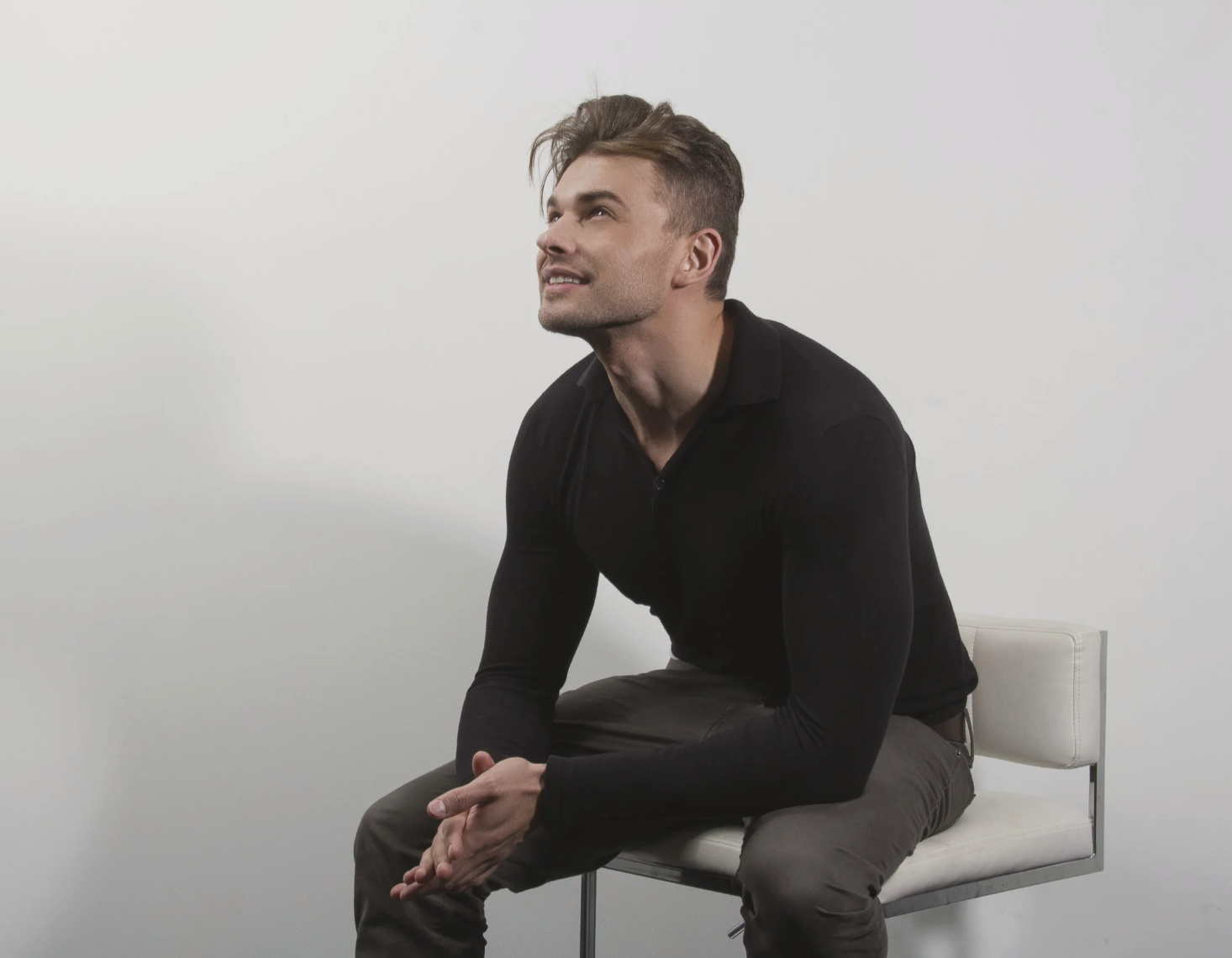 Kaden James seated in a minimalist studio, looking upward in a reflective pose for life coaching, personal growth, clarity, and mindset transformation.