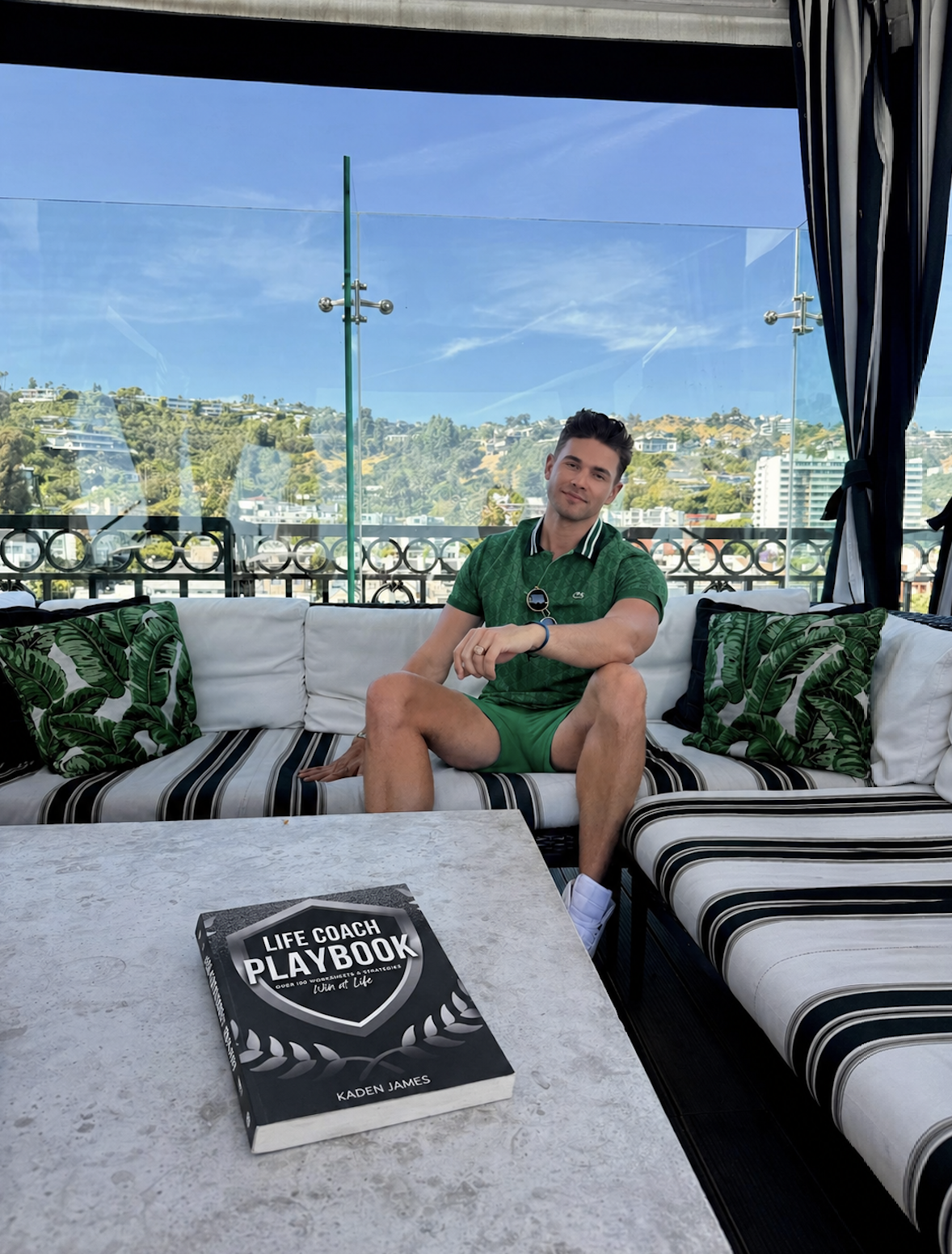 Kaden James, author and life coach, seated on a luxury outdoor lounge with his Life Coach Playbook, representing personal growth, confidence coaching, energy alignment, and authentic self-expression.