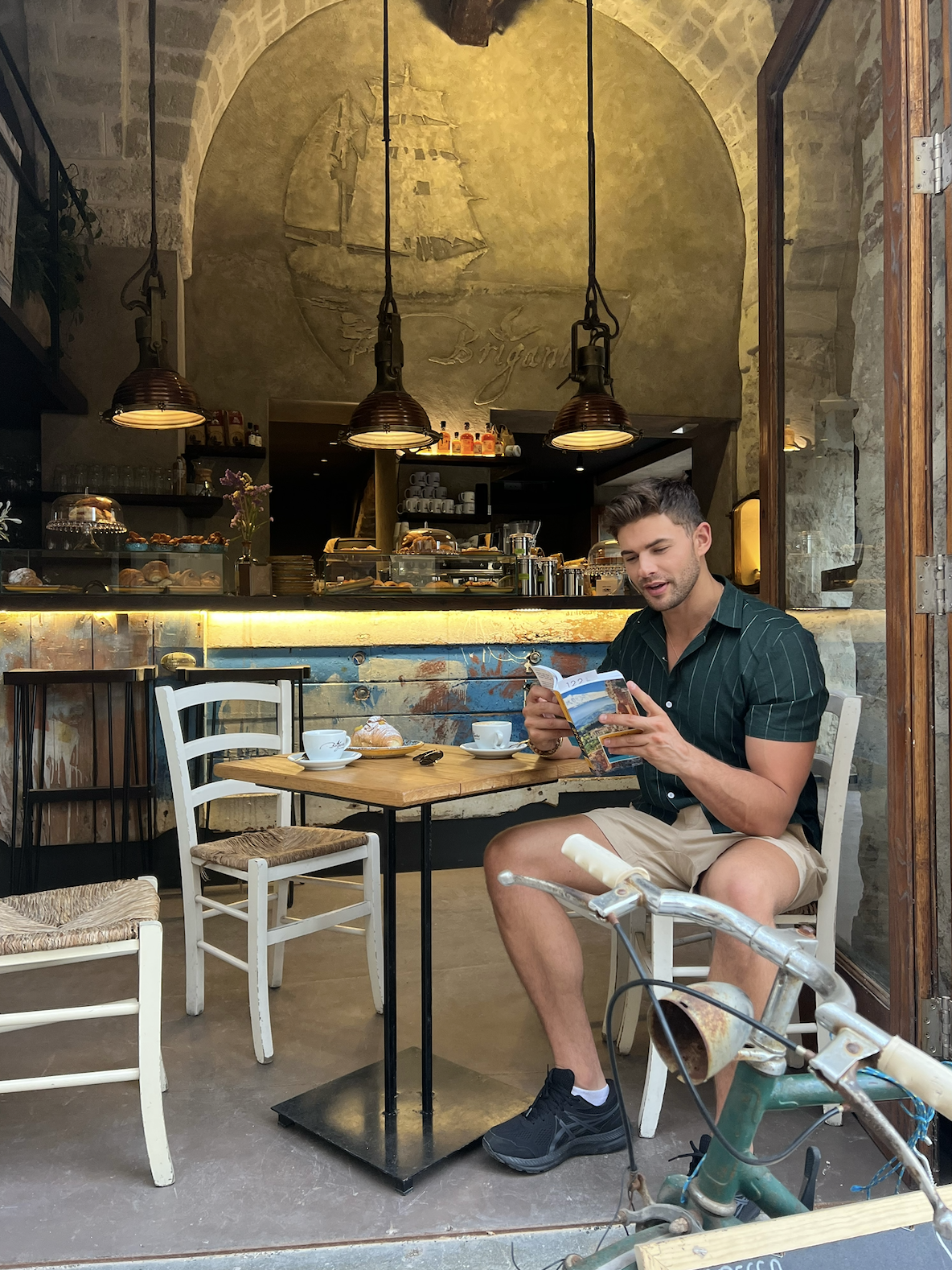 A picture of Life Coach Kaden James seated in a cafe in Italy reading the Rick Steves Italian Travel Guide book on his first day in Italy.