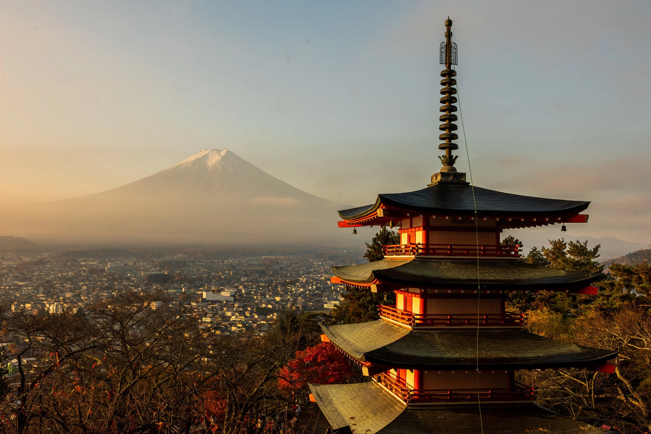 A traditional Japanese pagoda in the foreground with Mount Fuji in the background, set against a sunset sky.