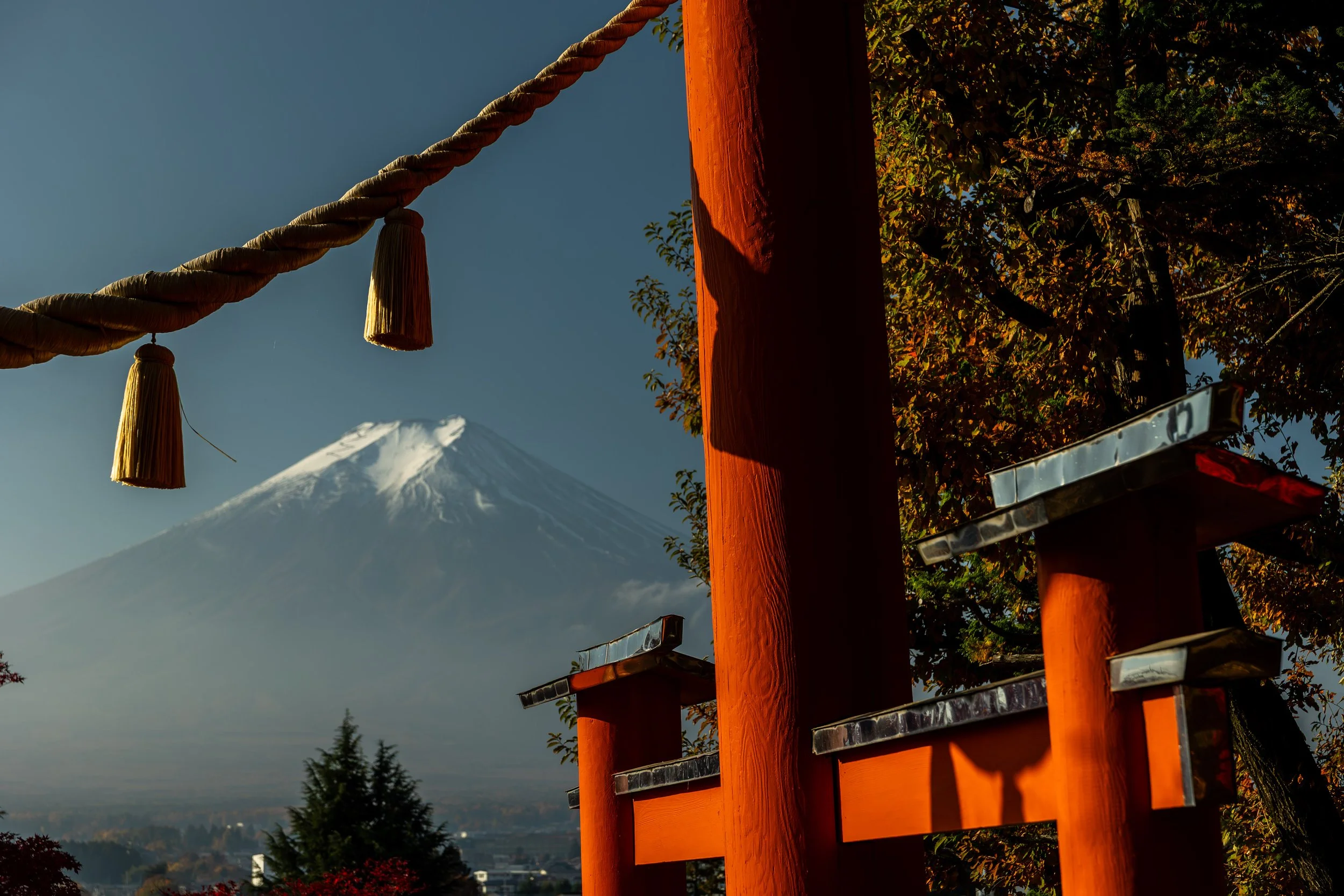 A traditional Japanese torii gate with a shimenawa rope and tassels, with Mount Fuji in the background under a clear sky.