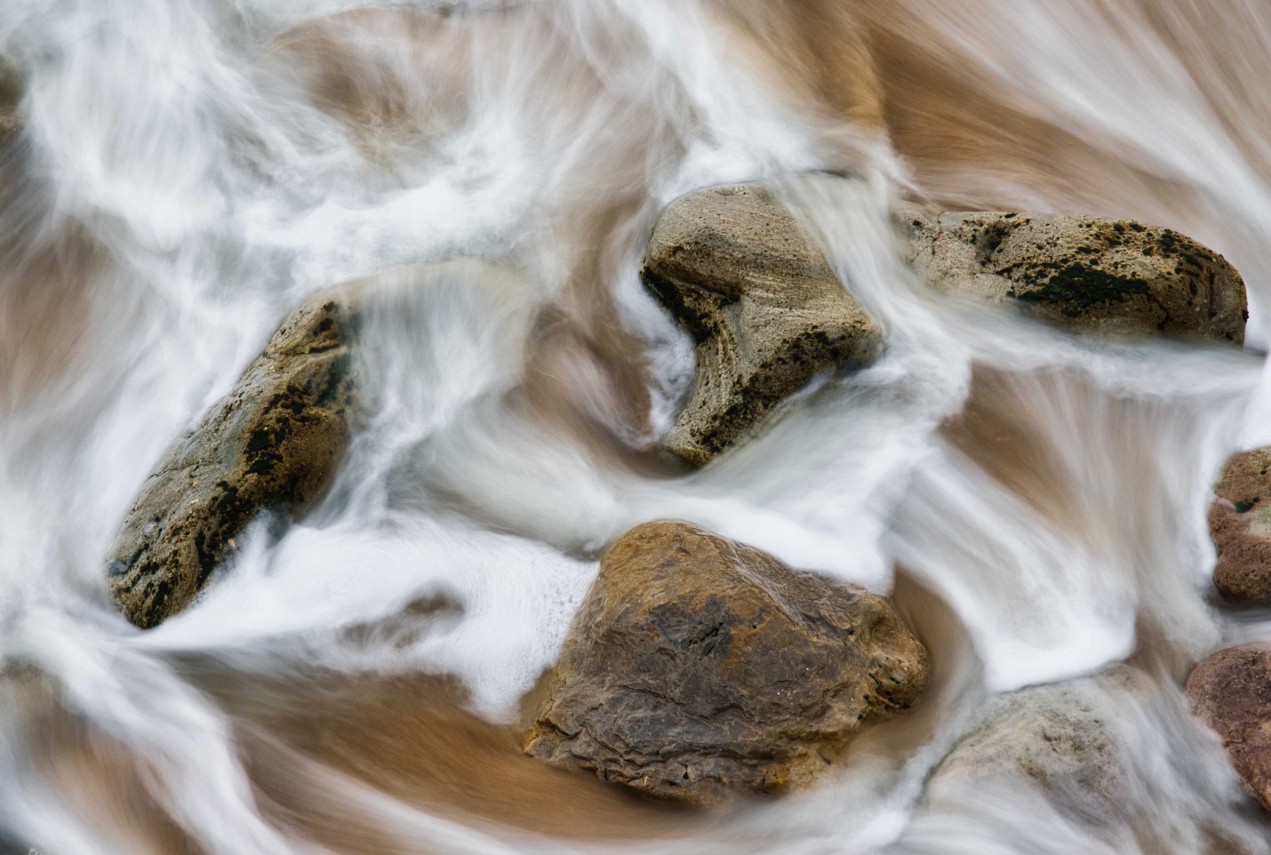 Flowing water around rocks in a river or stream, captured with a long exposure.