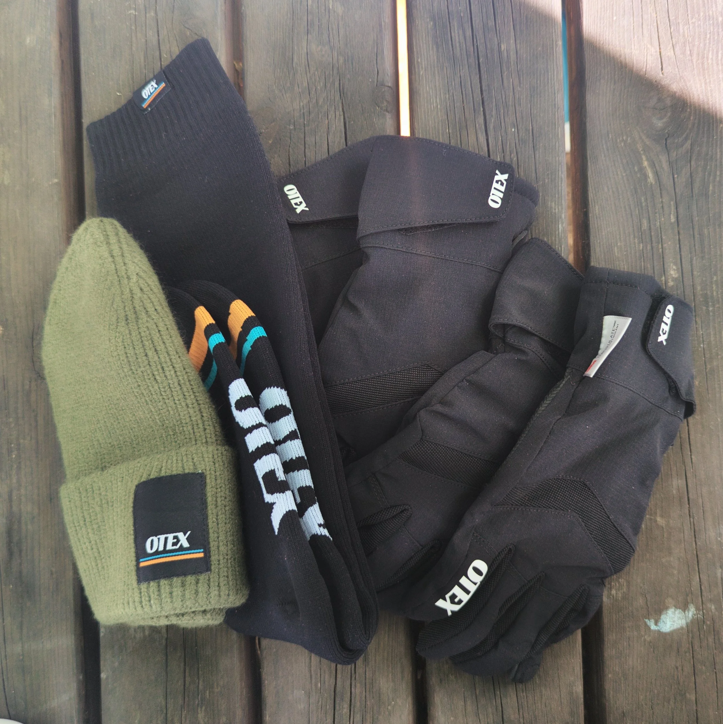 A green knit glove, two pairs of black and white gloves, and three black Otix-branded gloves, all placed on a wooden surface.