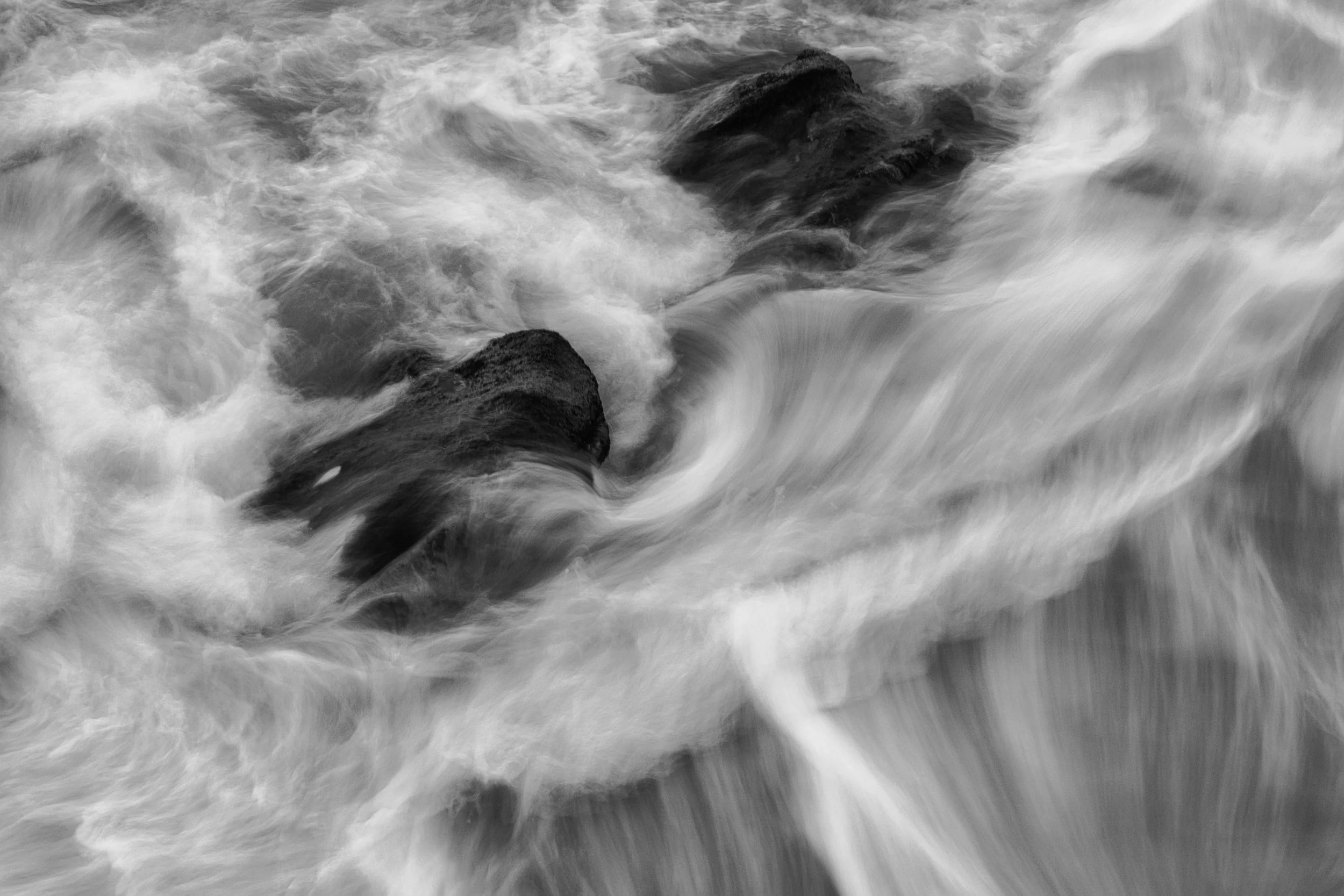 Black and white photograph of turbulent water flowing over rocks in a river or stream.