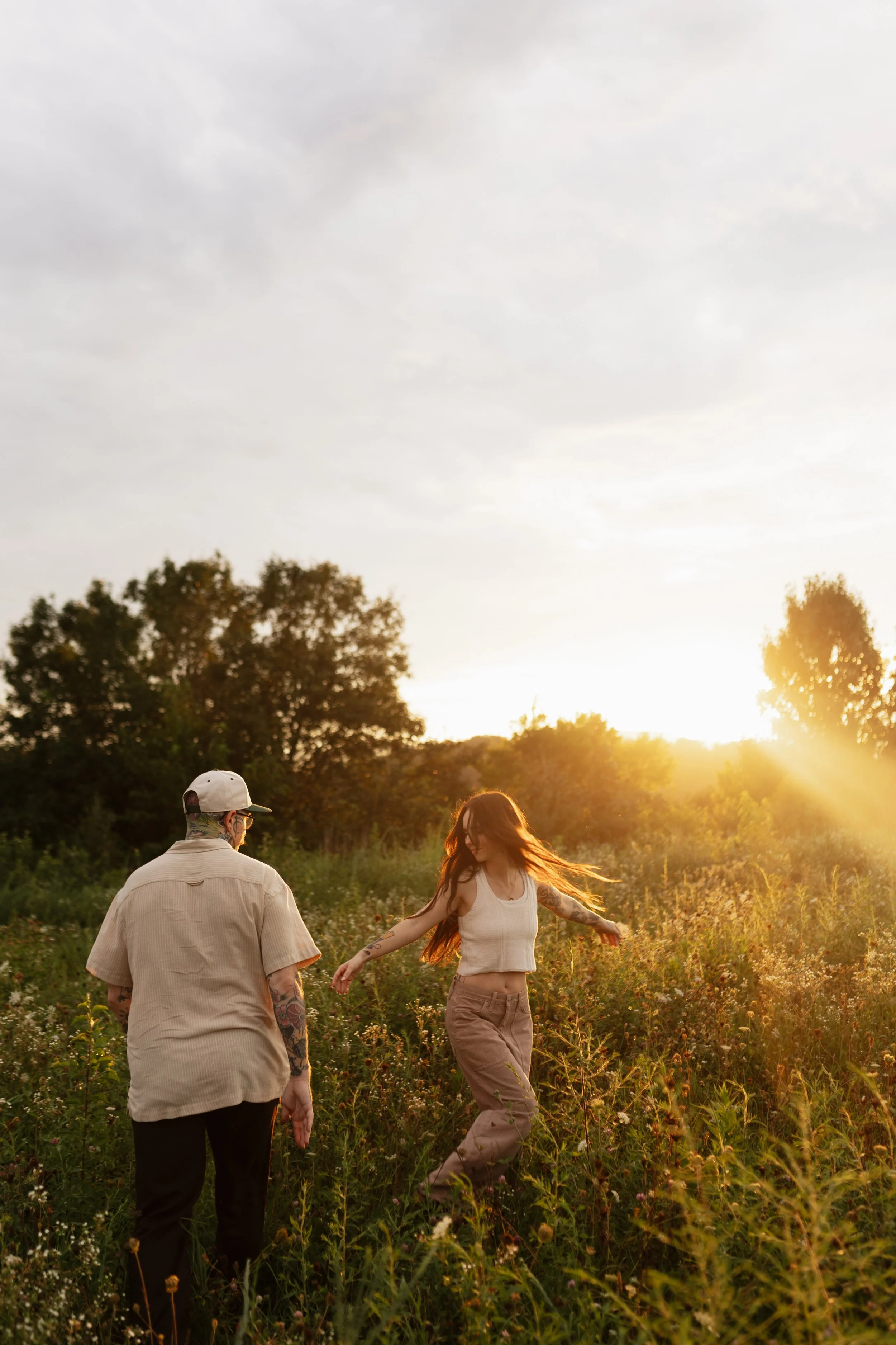 A man and a woman are walking in a field during sunset, with trees in the background.