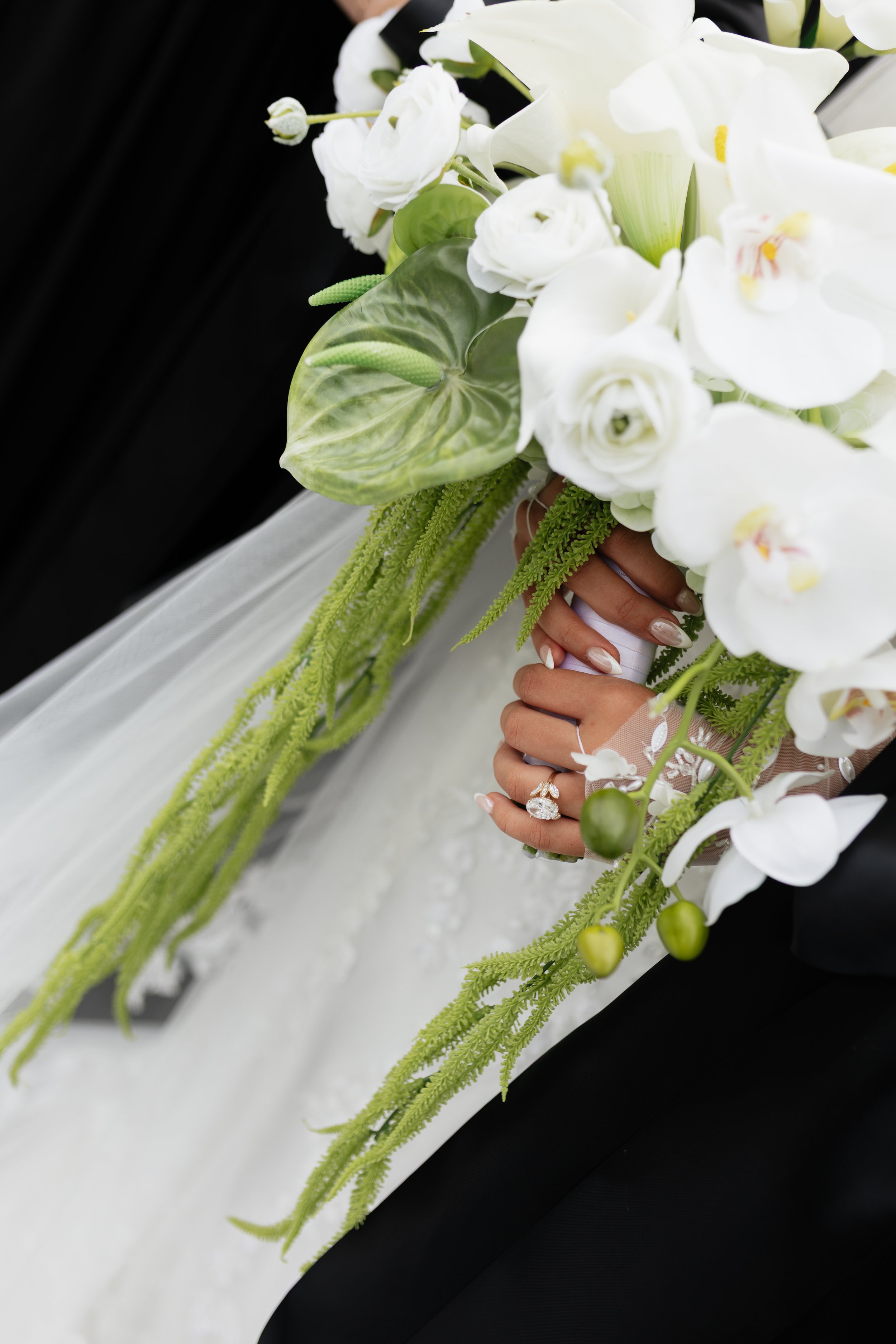 Close-up of a bride holding a cascading bouquet of white orchids, calla lilies, and greenery with a blurred background.