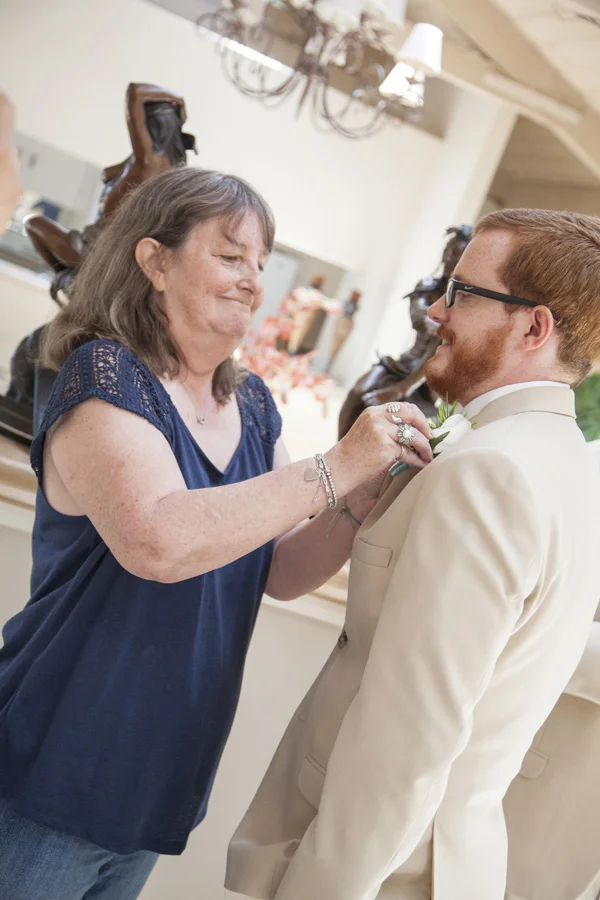 The grooms mother is smiling as she pins on the corsage