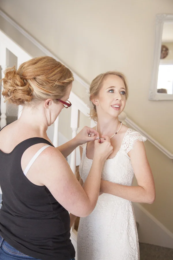 The bride is getting her necklace put on.