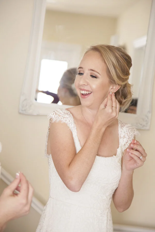 The bride is smiling as she puts her earring on.