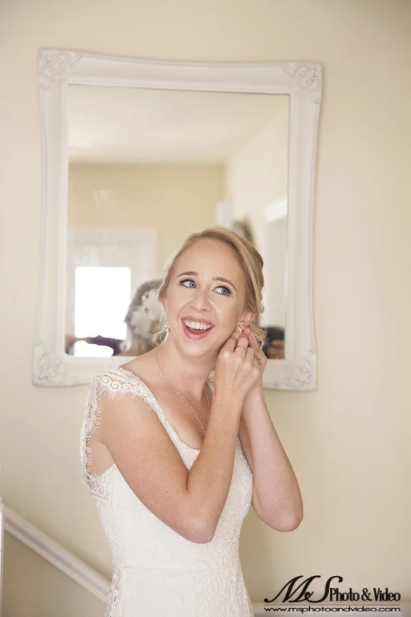 The bride is smiling as she puts her earring on