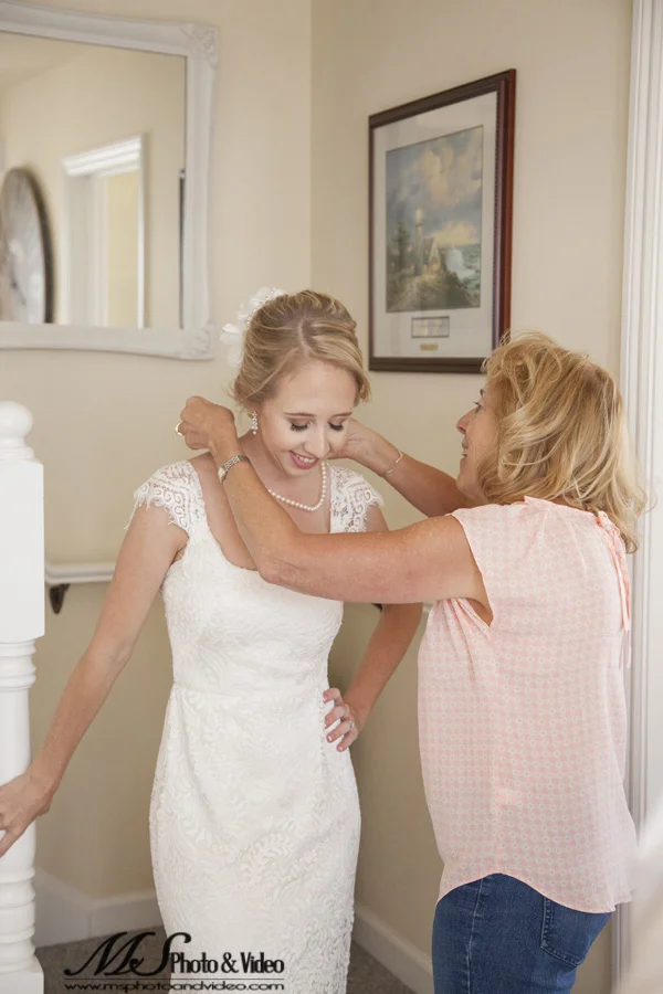The bride's mother is putting the necklace on the bride.