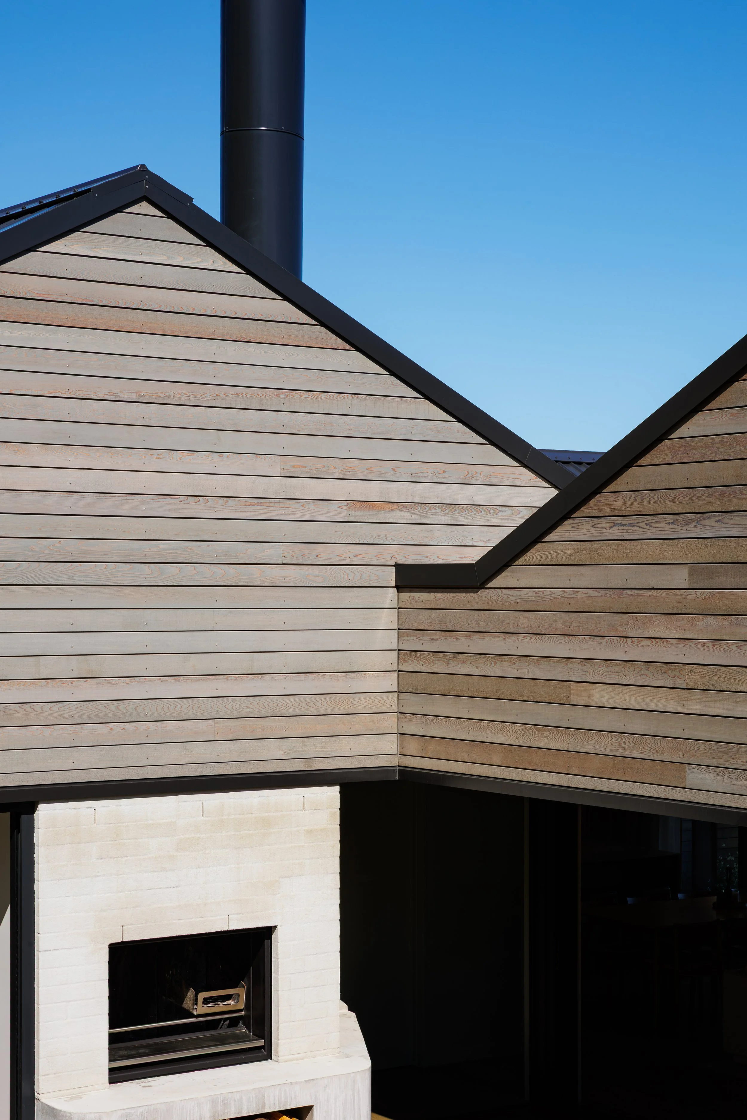 Close-up of a modern house exterior featuring wooden siding, a chimney, and a fireplace.