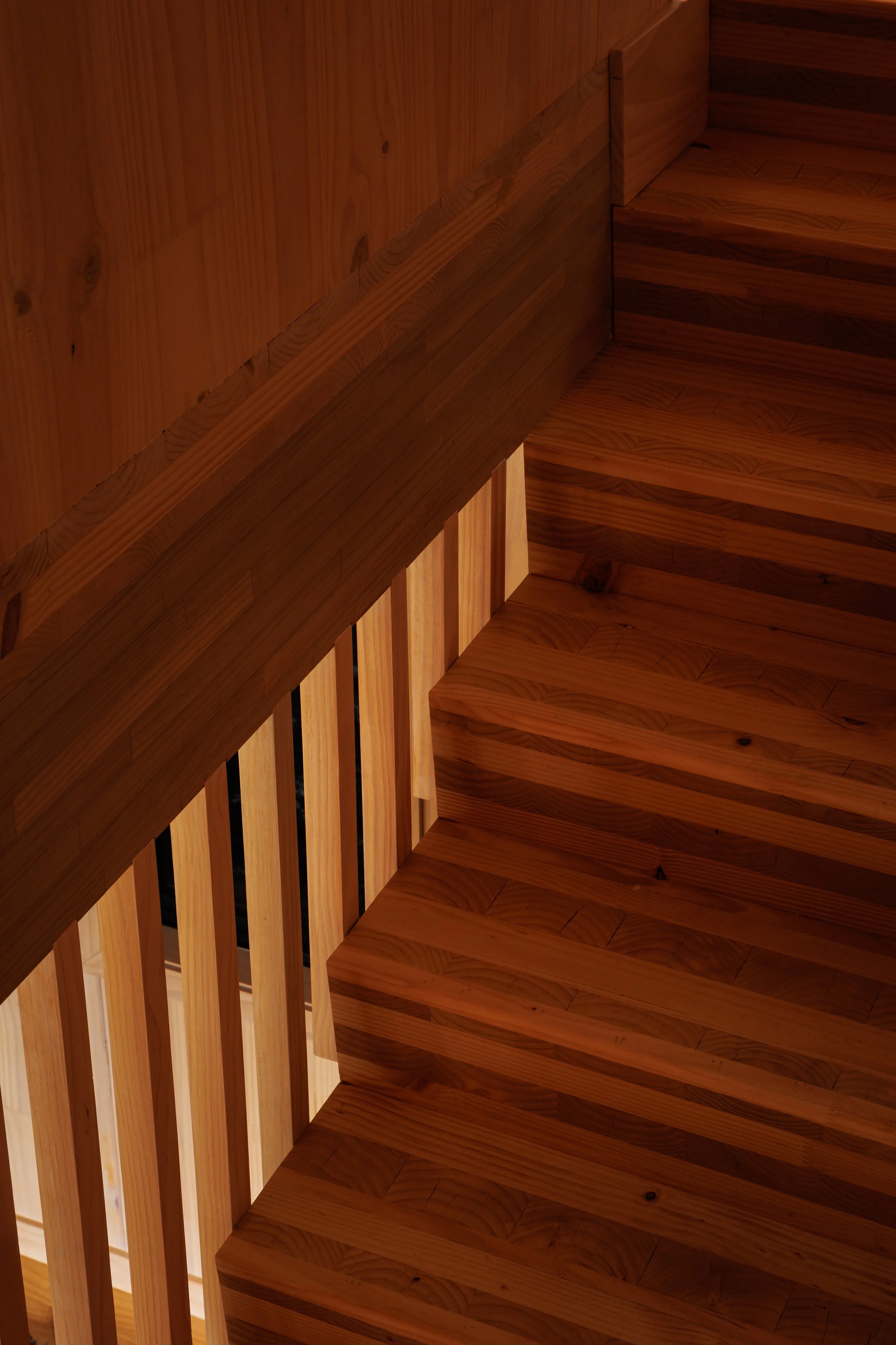 Close-up view of a wooden staircase with a curved railing and vertical balusters, showcasing the natural wood grain.
