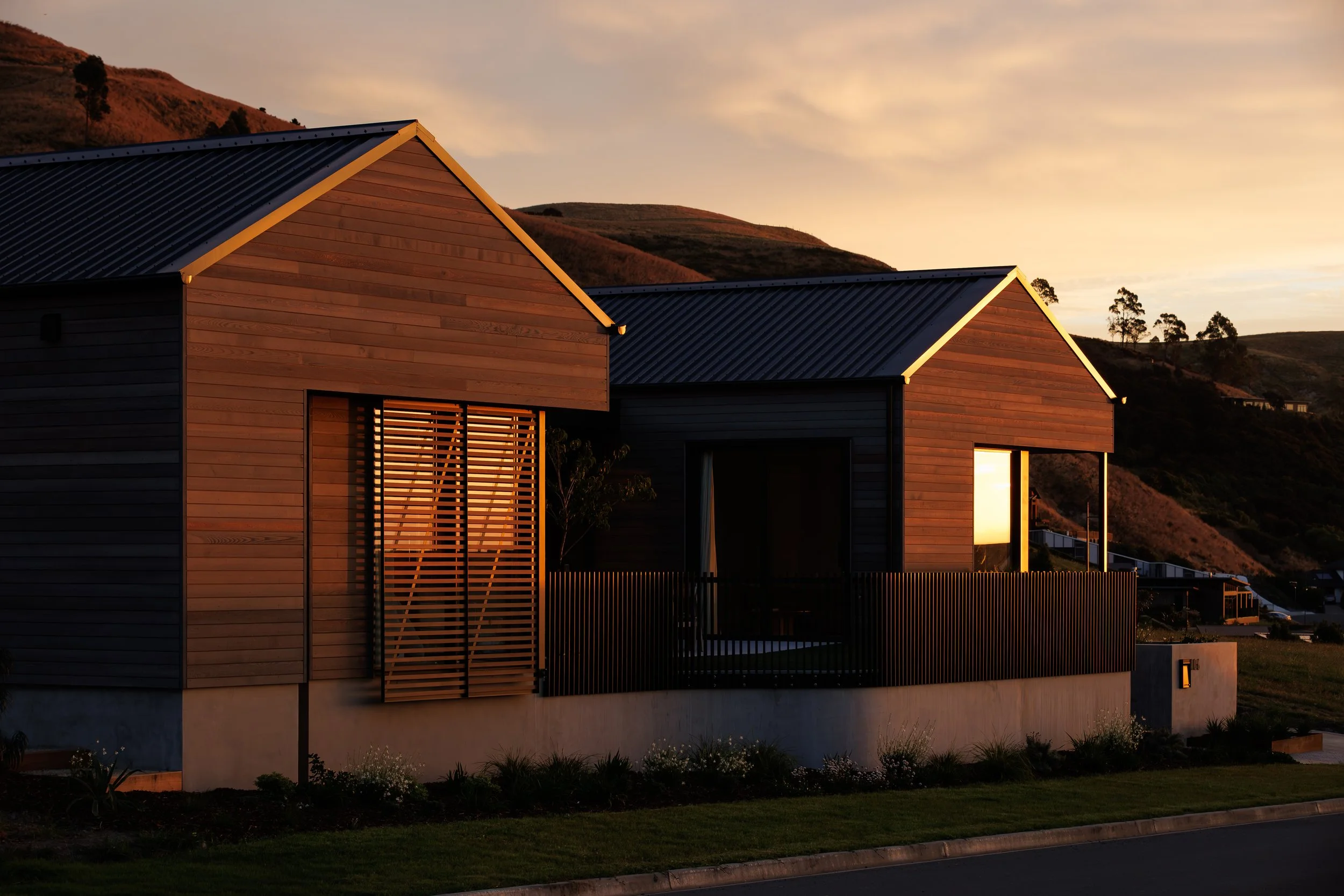 Modern wooden houses with metal roofs at sunset in a hilly landscape.