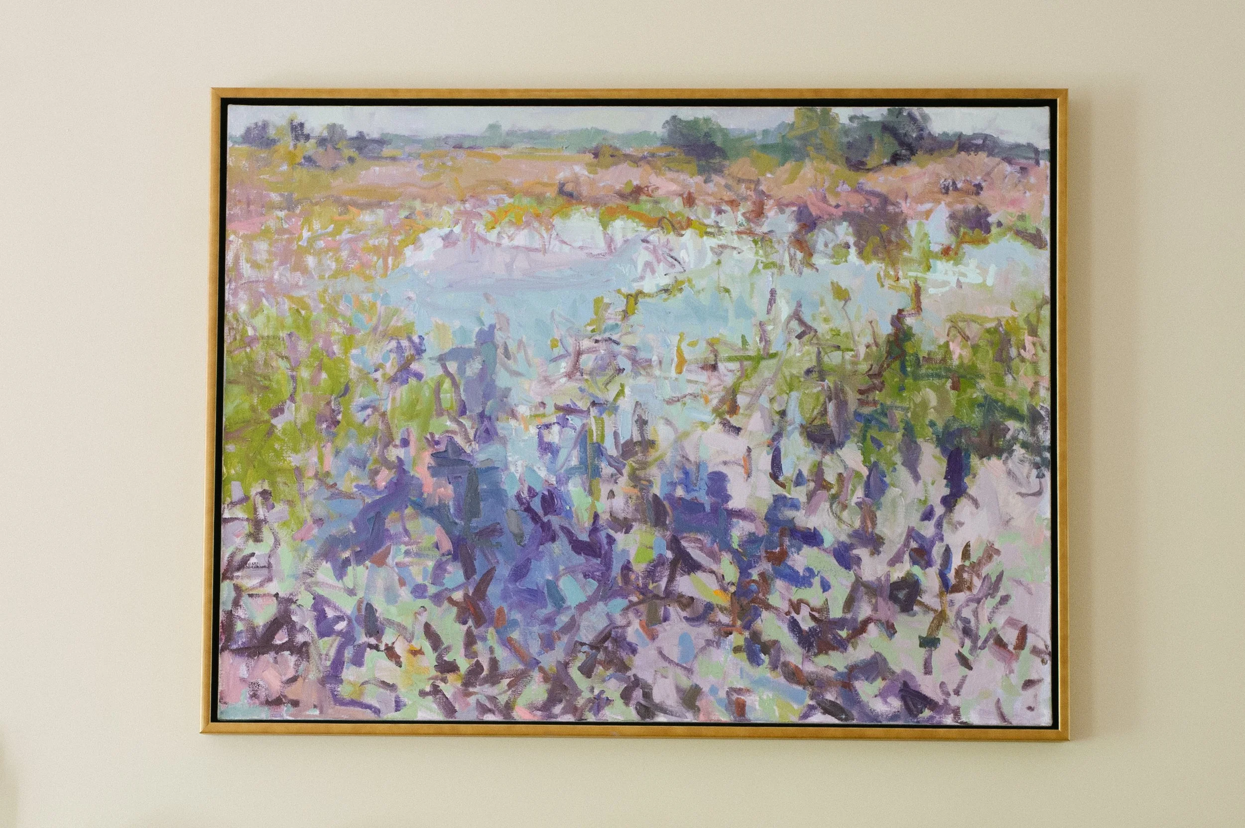 An abstract landscape painting with a river, fields, and trees in pastel colors, framed and hanging on a white wall.
