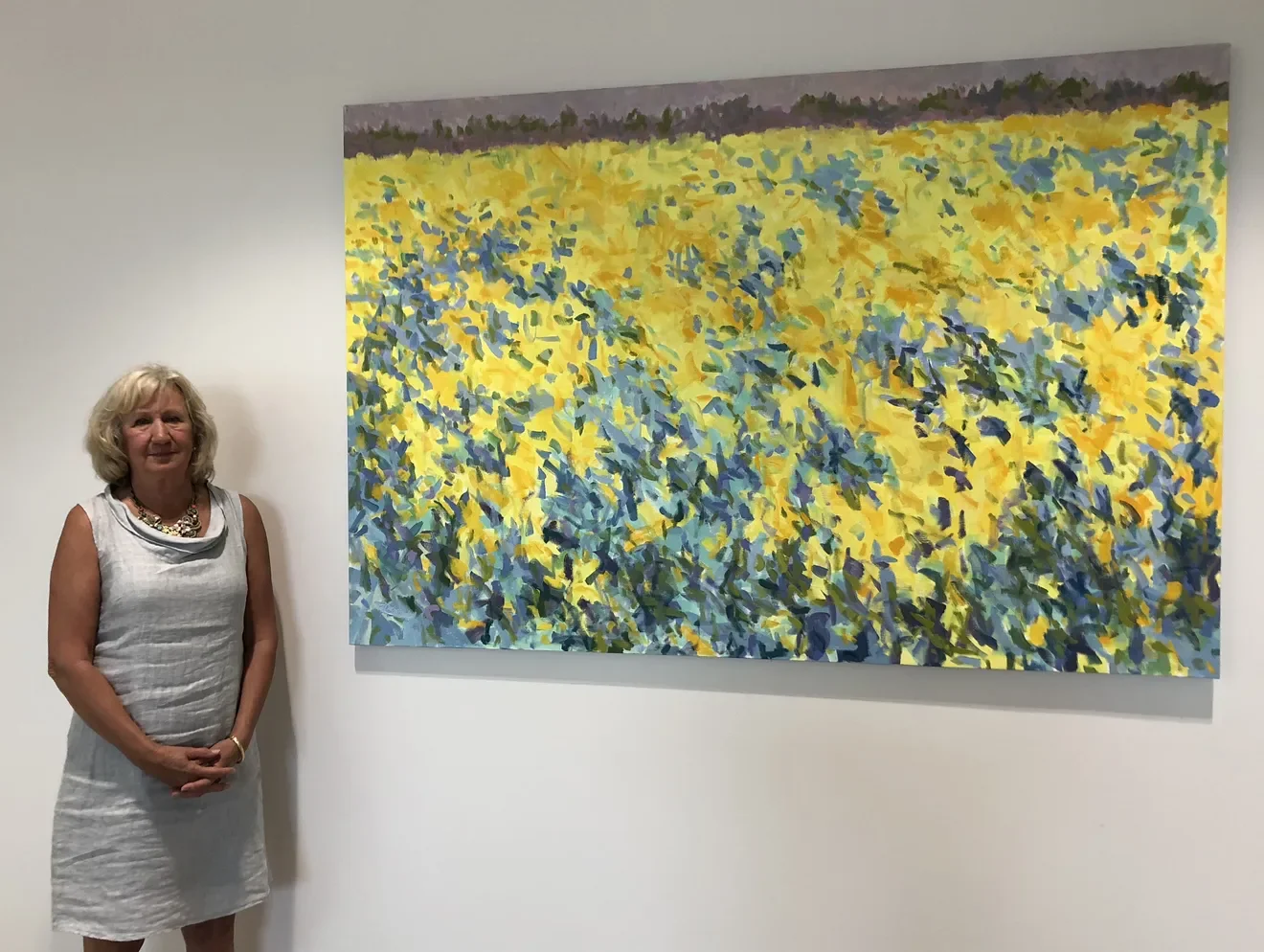 Priscilla standing next to a large, colorful painting of a field of yellow and blue flowers.