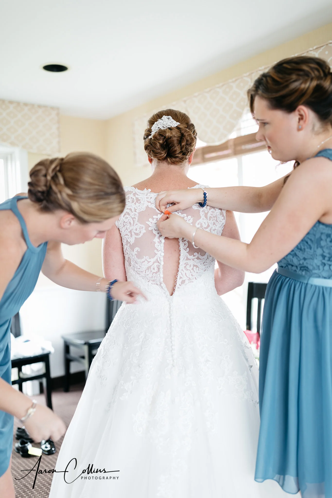 Bridesmaids helping the bride button up the back of her wedding dress.
