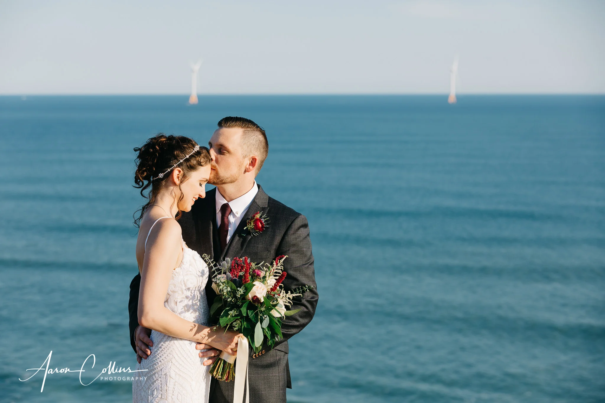 Groom kissing bride on the forehead on the cliffs at Mohegan Bluffs overlooking Block Island Sound.