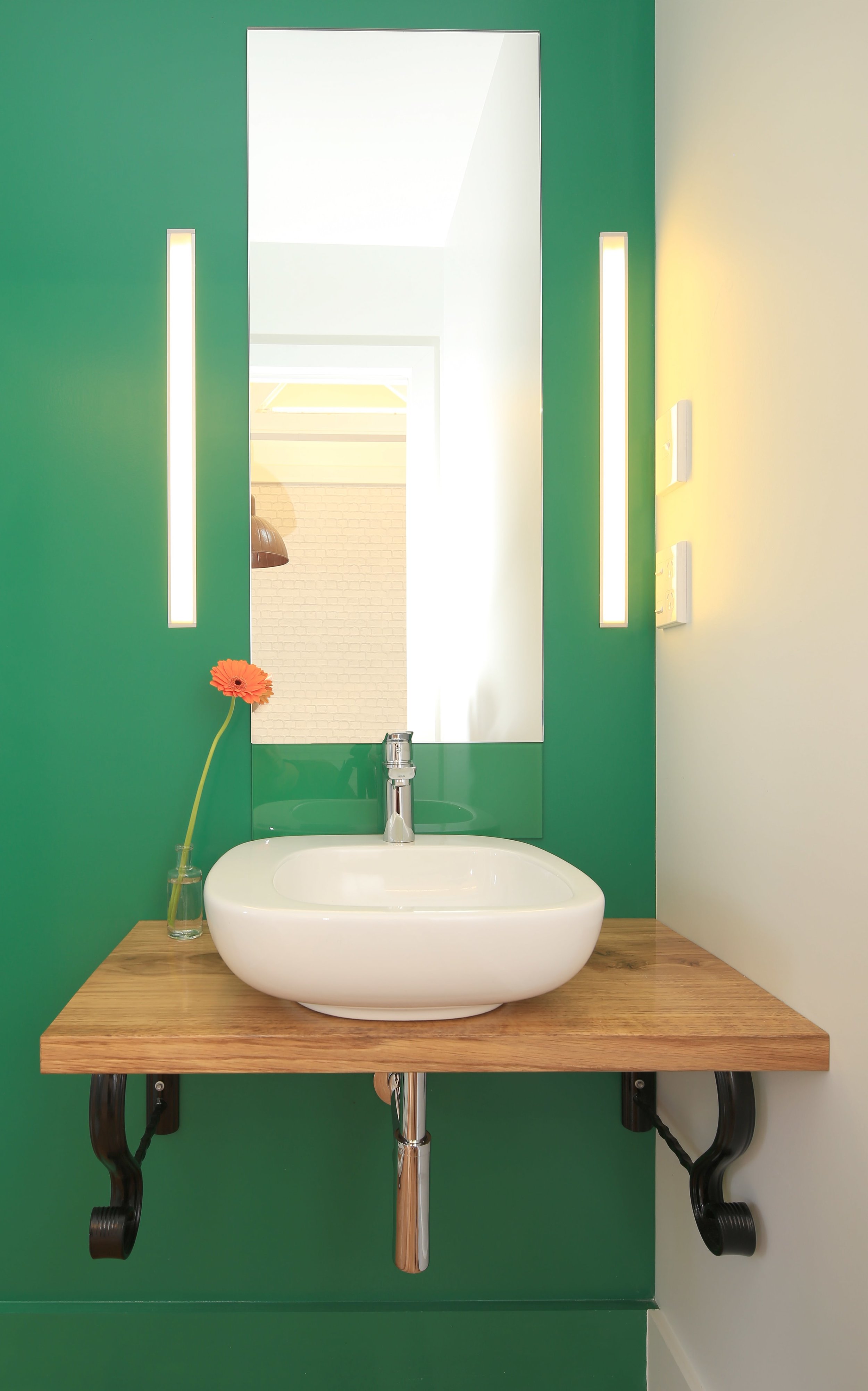 Green bathroom with white basin on wooden bench with rectangle mirror