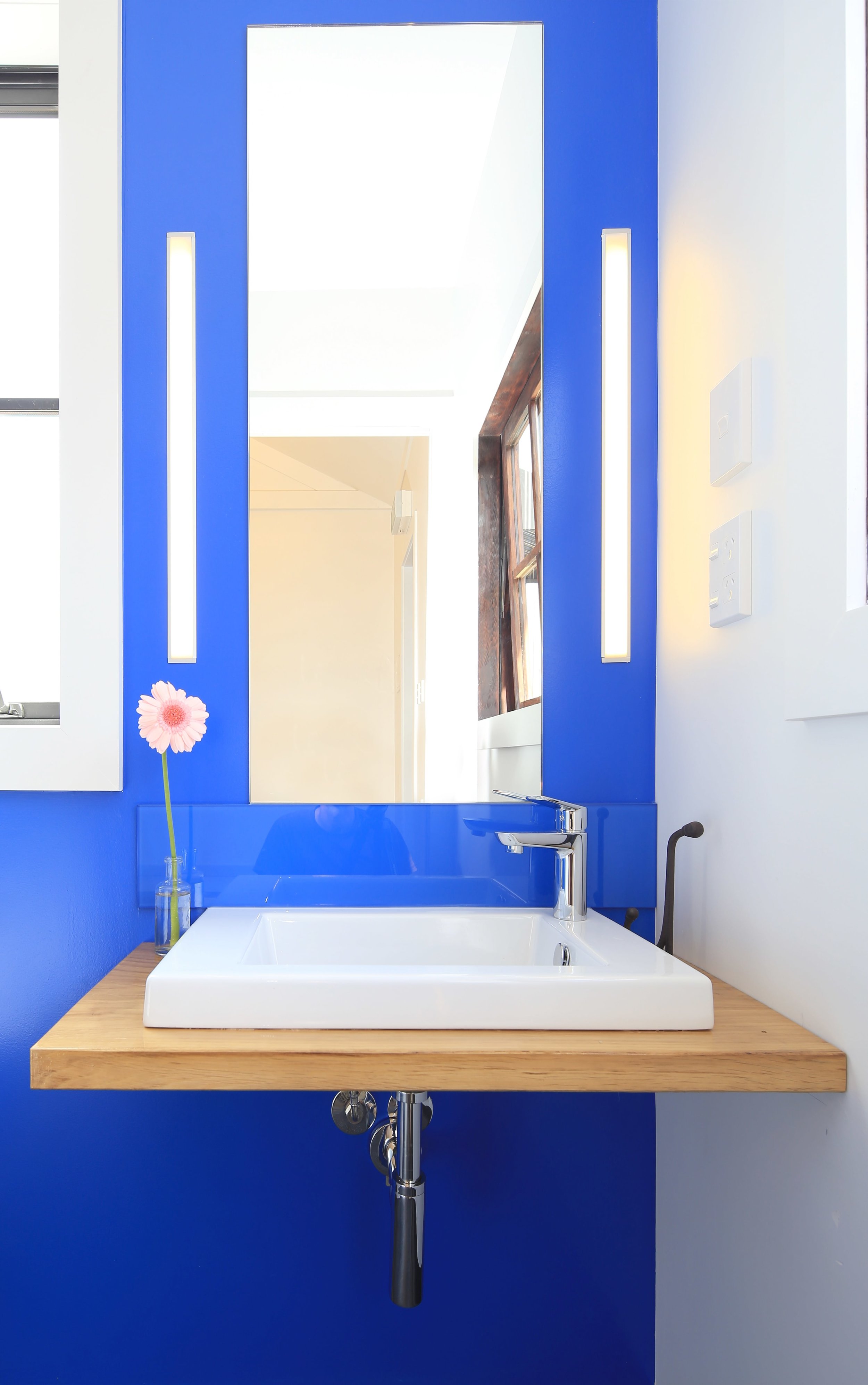 Blue bathroom wall with rectangle mirror and white basin