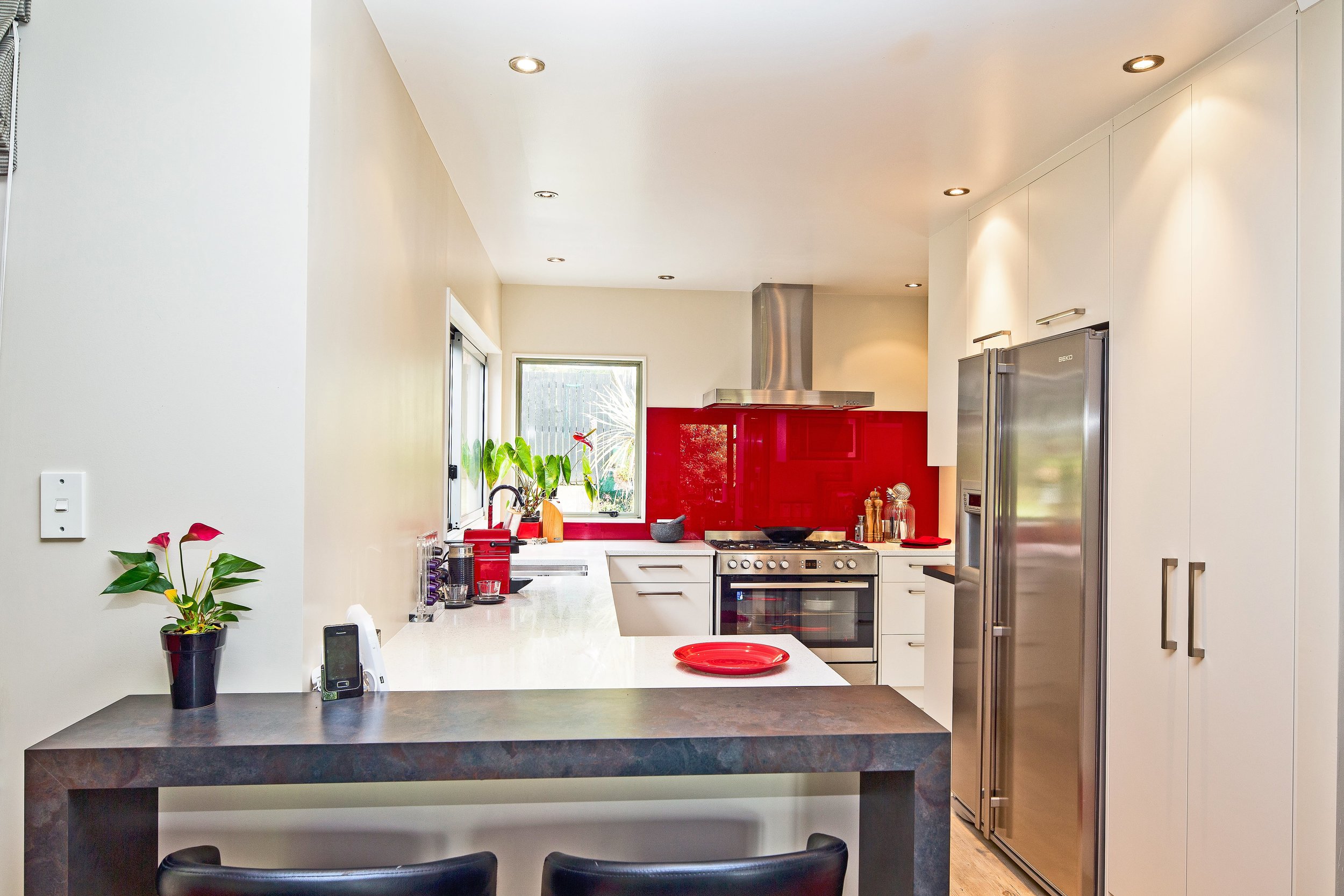 Galley style kitchen with red backpainted glass splashback adding pop of colour