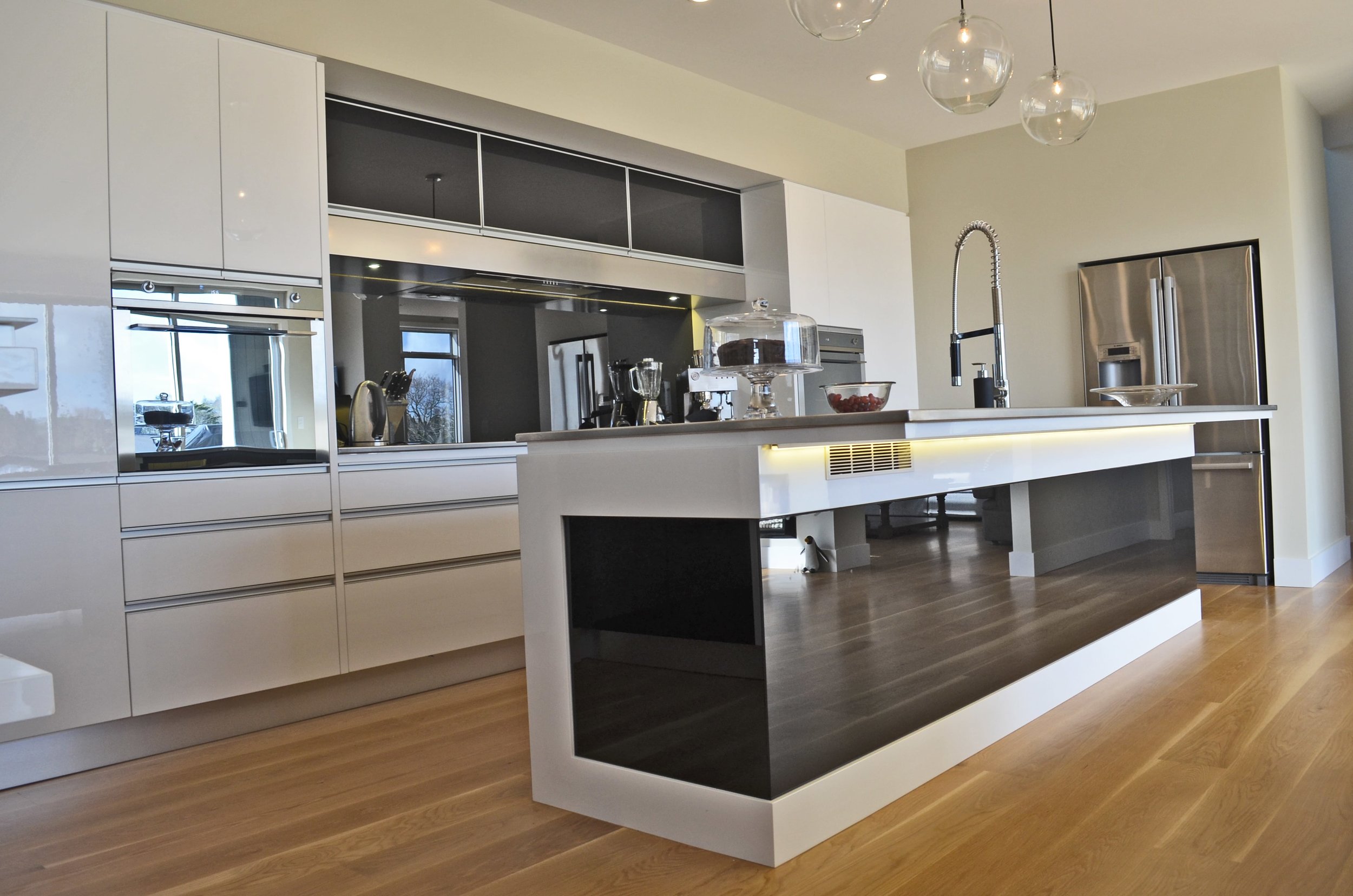 Galley kitchen with white cabinetry and black backpainted glass splashback and island back