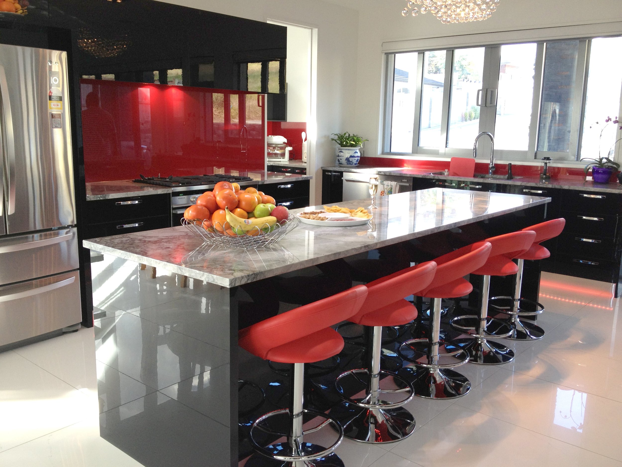Hi gloss dark cabinetry and red backpainted glass splashback with marble benchtop