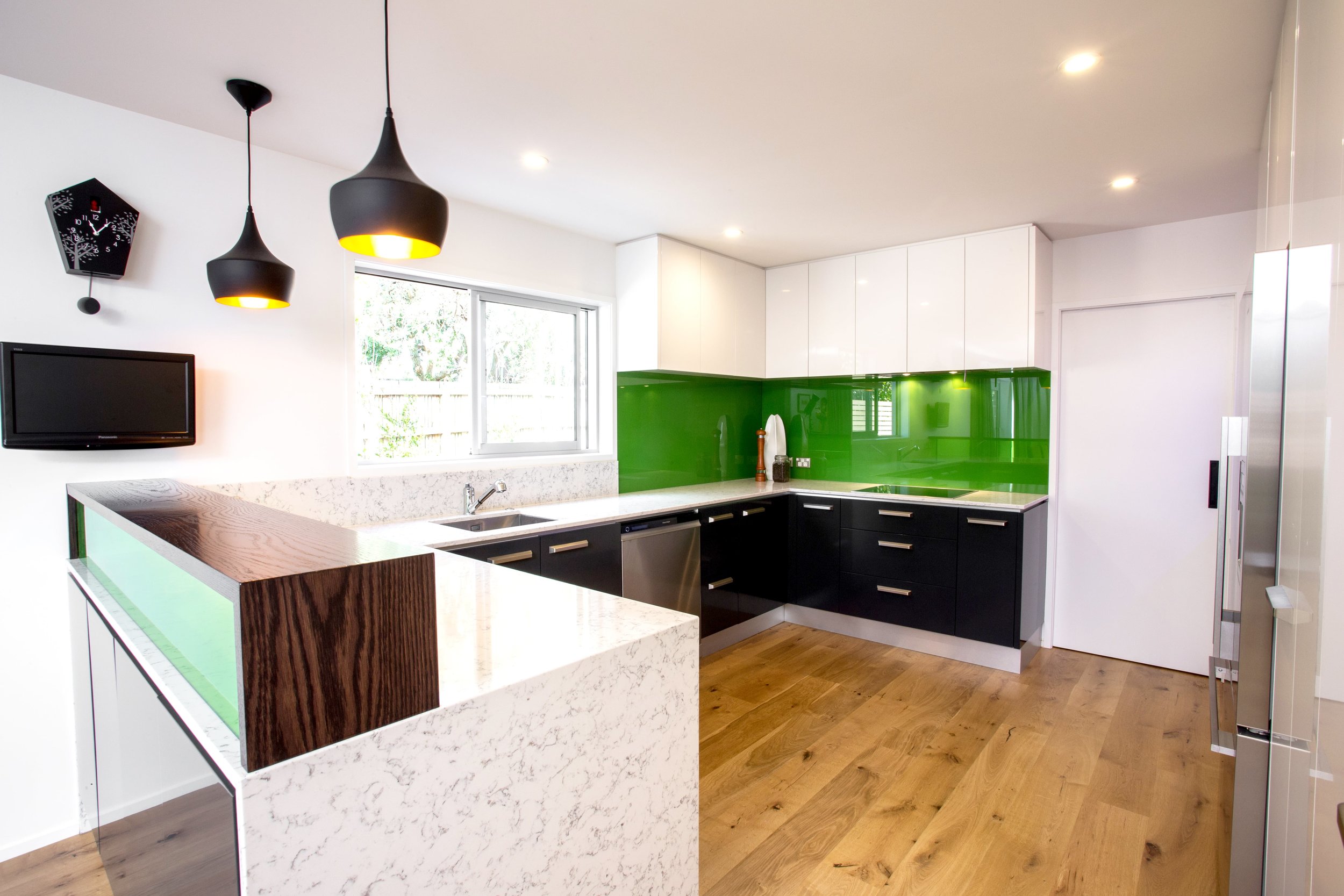 Kitchen with light-dark cabinetry with feature green glass splashback