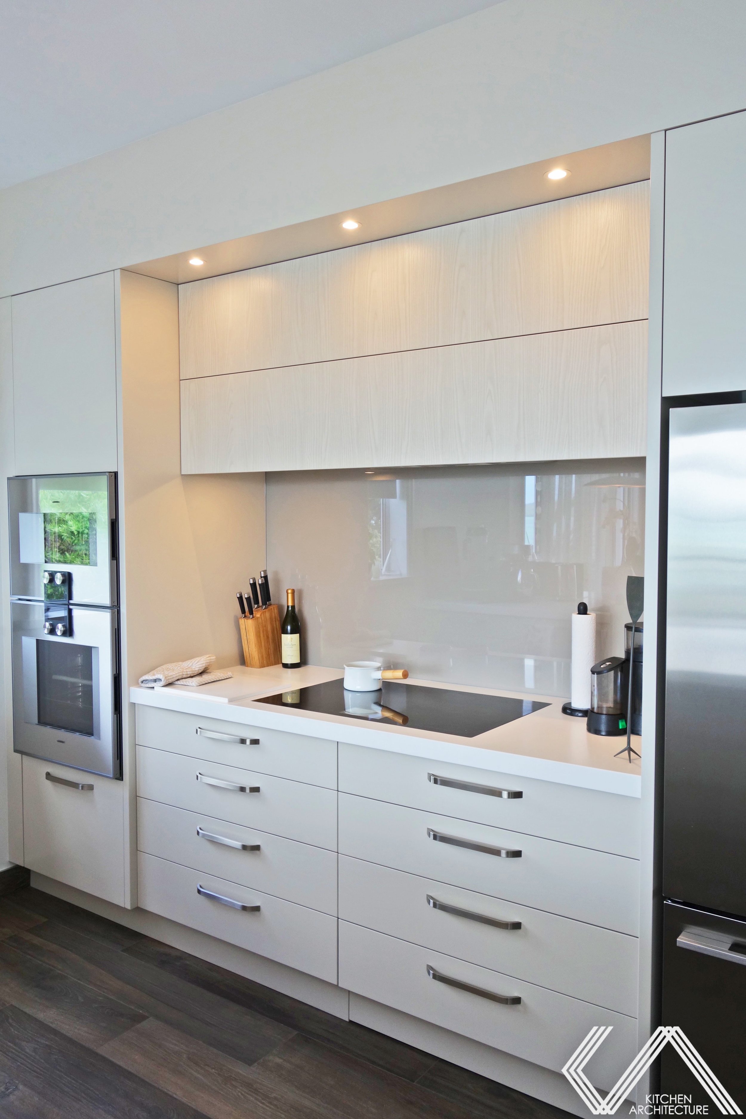 White kitchen with stainless handles and light grey glass splashback