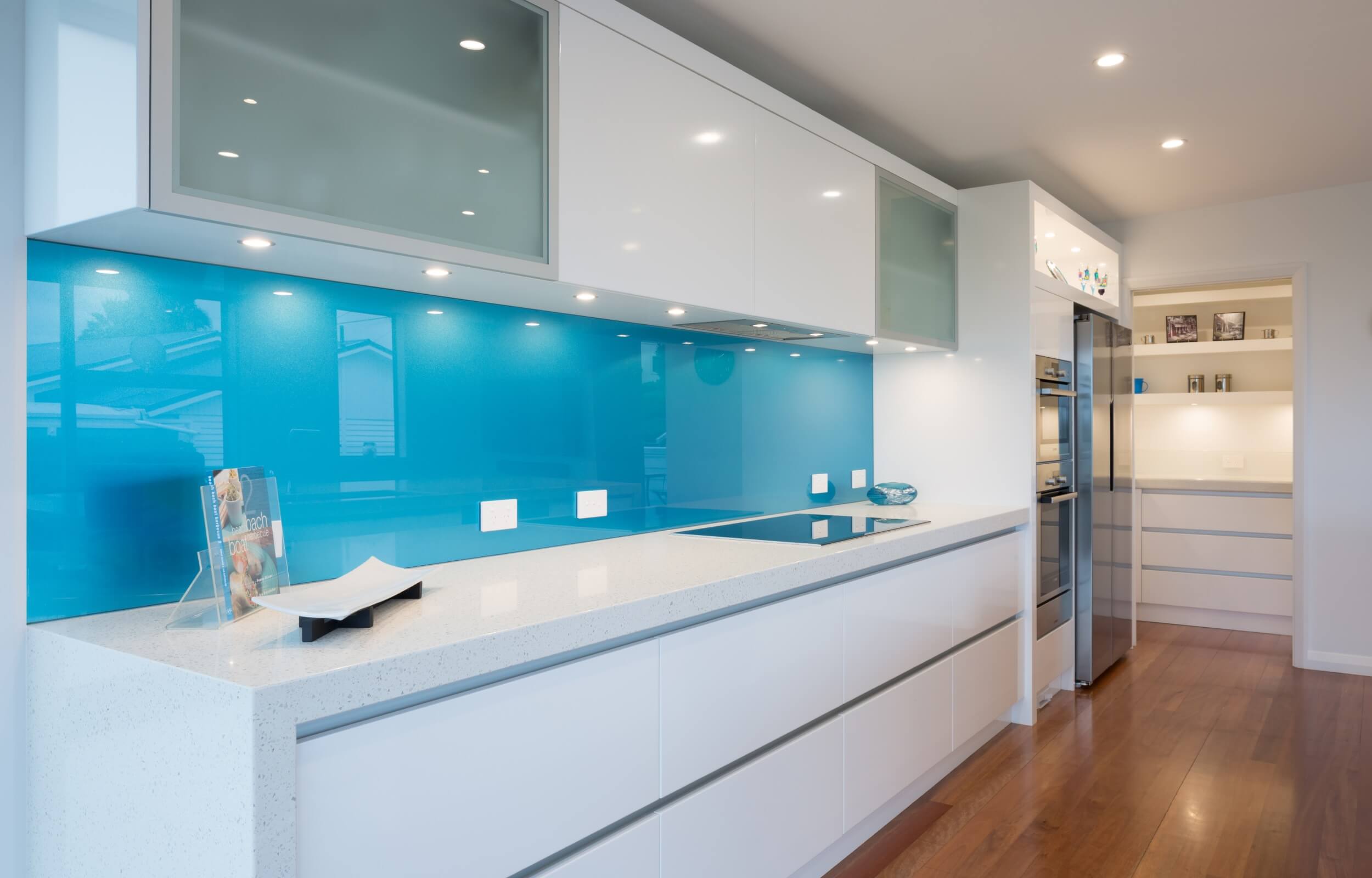 Metallic blue splashback in modern white kitchen with sucllery