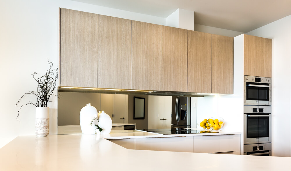 Mirrored glass splashback featured in light woodgrain apartment kitchen